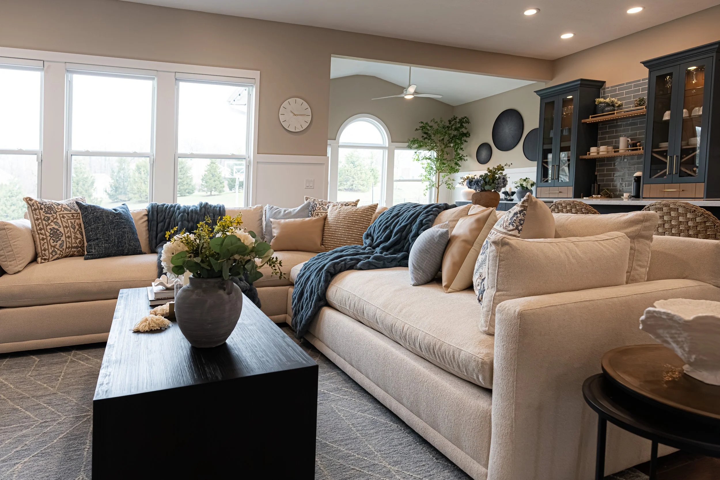 Living room with a cream sectional, layered blue accents, and a wall of windows with an arched transom in a Centerville home renovation.