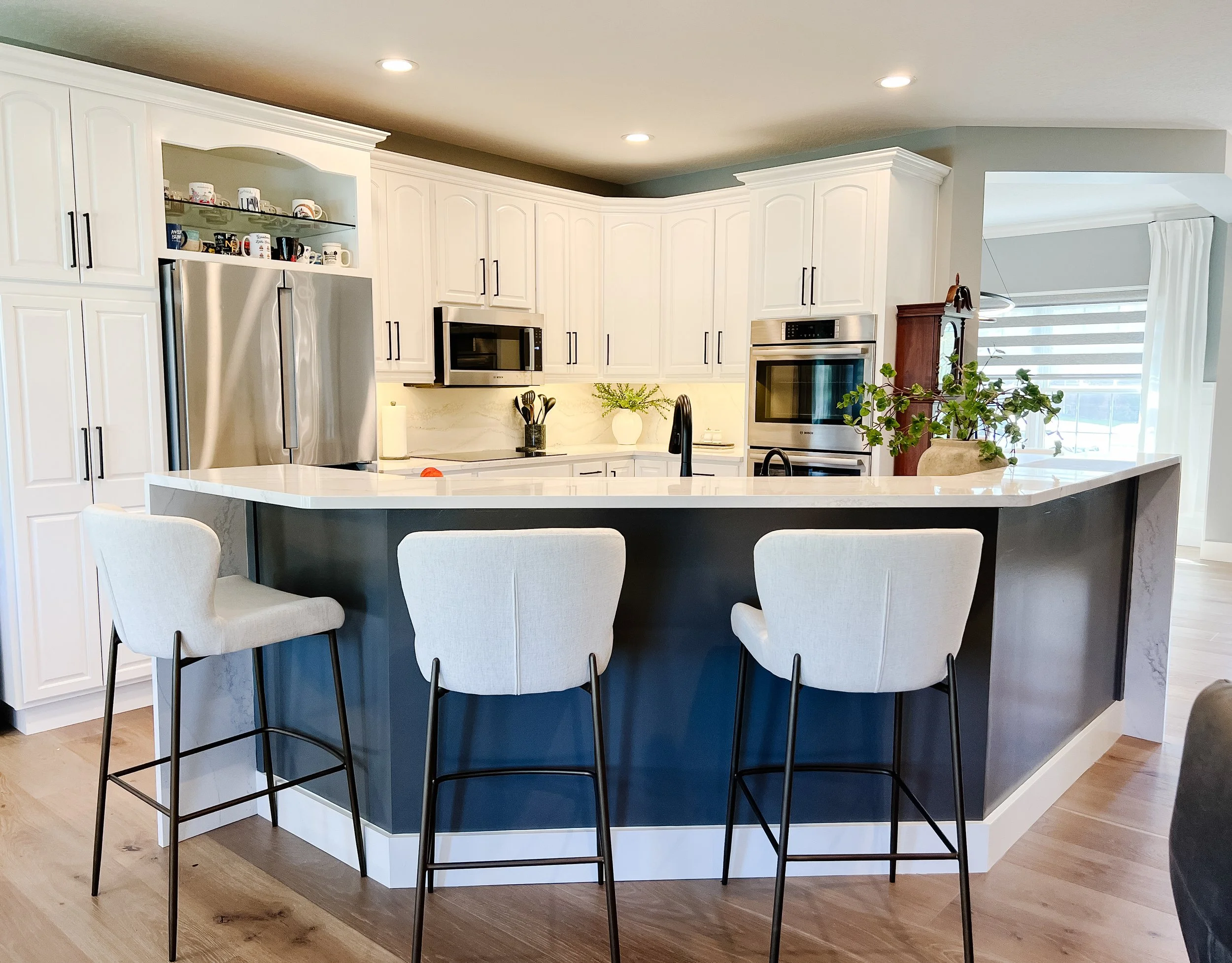 Renovated kitchen with white cabinetry, a navy island with quartz countertop and upholstered stools, stainless appliances, and light wood flooring in a Xenia, Ohio home