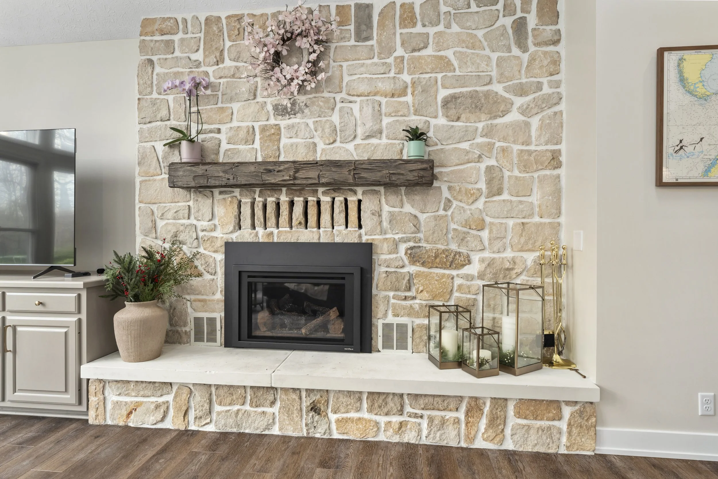 Floor-to-ceiling stone fireplace with reclaimed wood beam mantle, raised hearth, and a new gas insert in a renovated living room