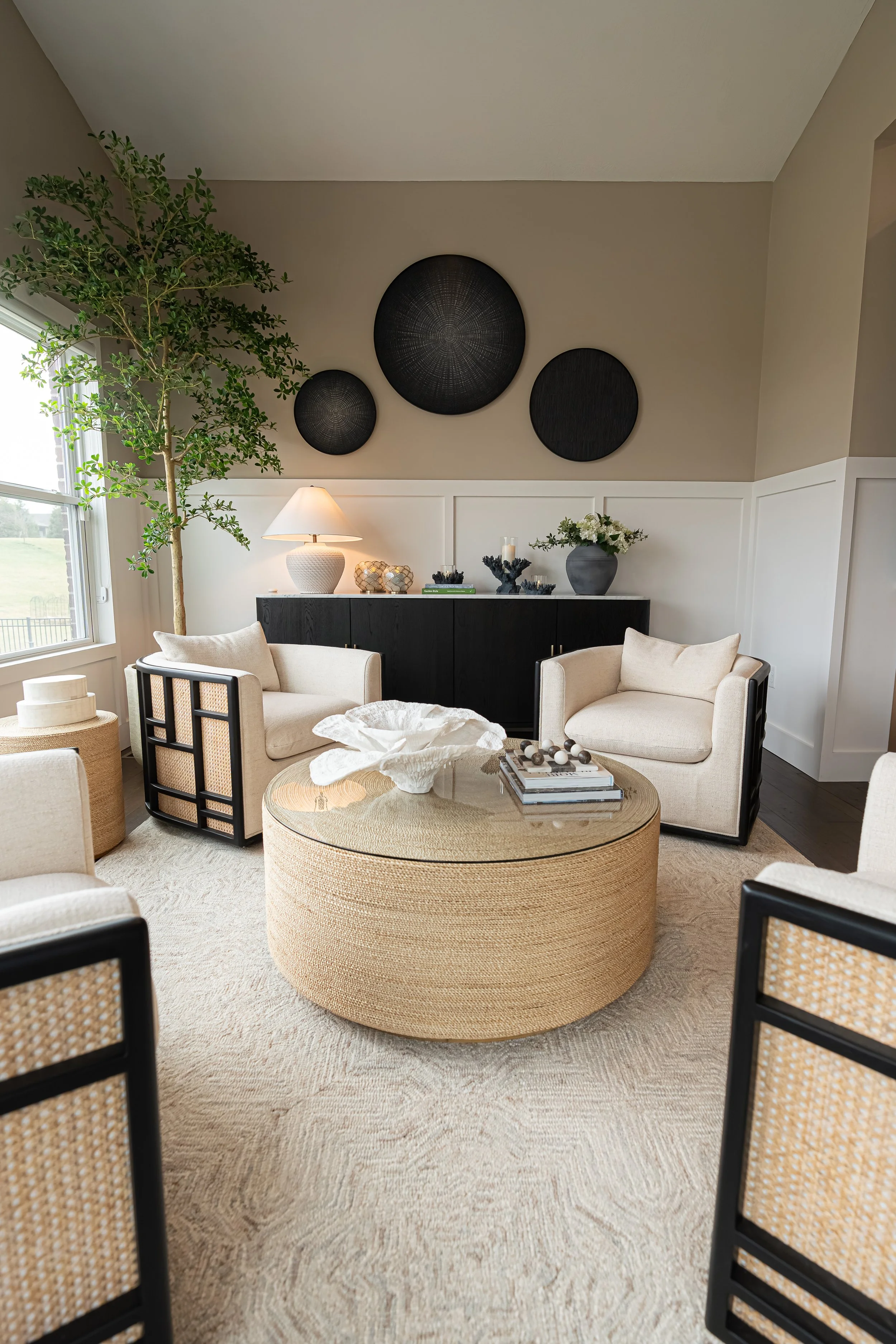 Bright sitting room with cream and cane accent chairs around a round woven drum coffee table in a Centerville home renovation.