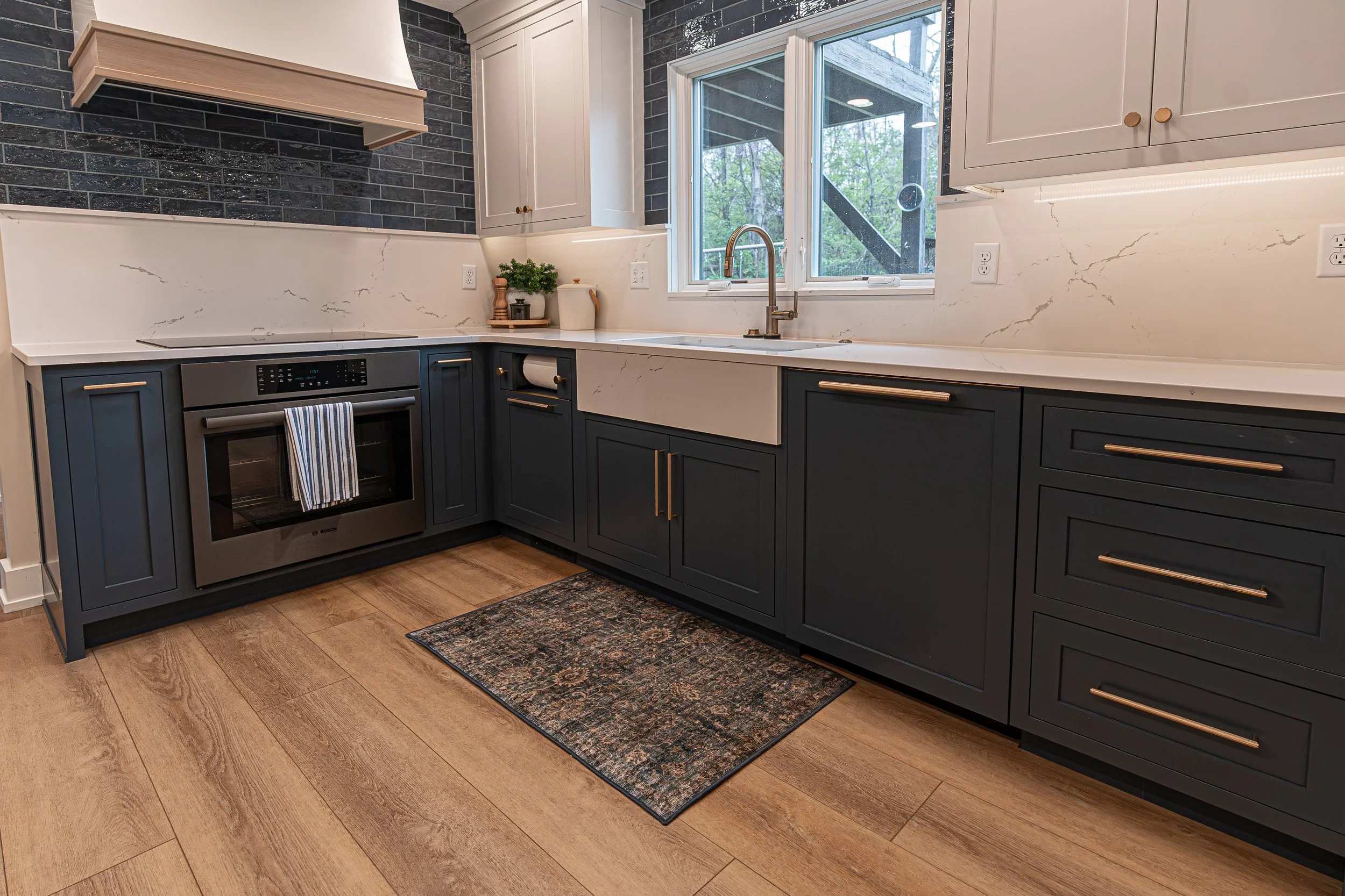 Farmhouse apron-front sink with a brass faucet and marble backsplash beneath a window in a Centerville kitchen remodel.