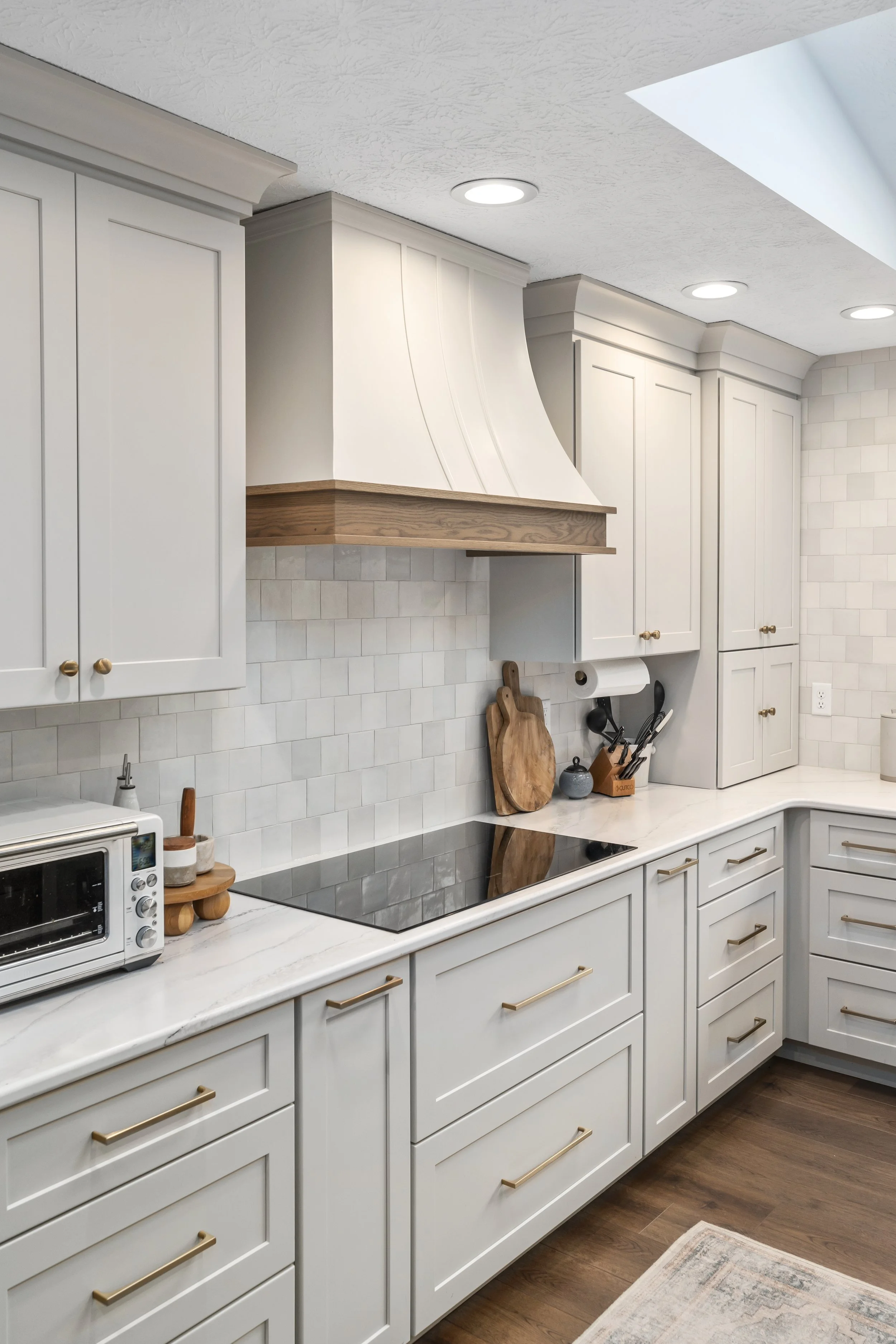 Custom curved range hood with stained wood accent band over an integrated cooktop, white tile backsplash, and quartz countertops