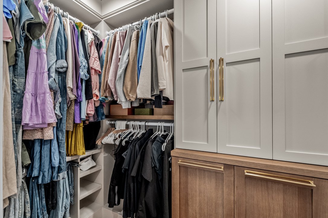 Custom closet corner with double-hung clothing rods, built-in white cabinetry, and wood drawers with gold hardware in a Xenia, Ohio master suite