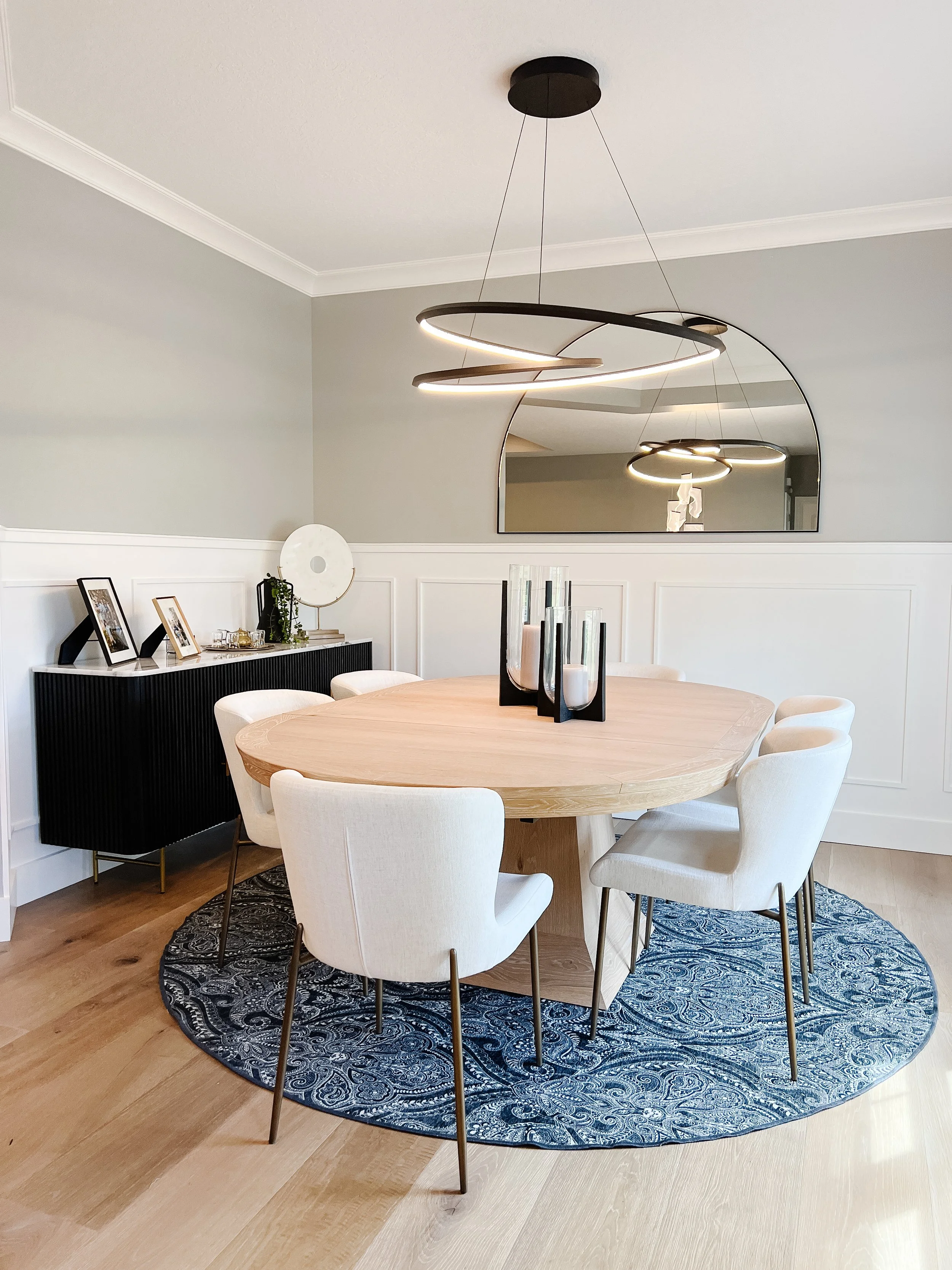 Eat-in dining area with a round wood table, upholstered chairs, a sculptural ring chandelier, board-and-batten wainscoting, and a patterned rug in a Xenia, Ohio home