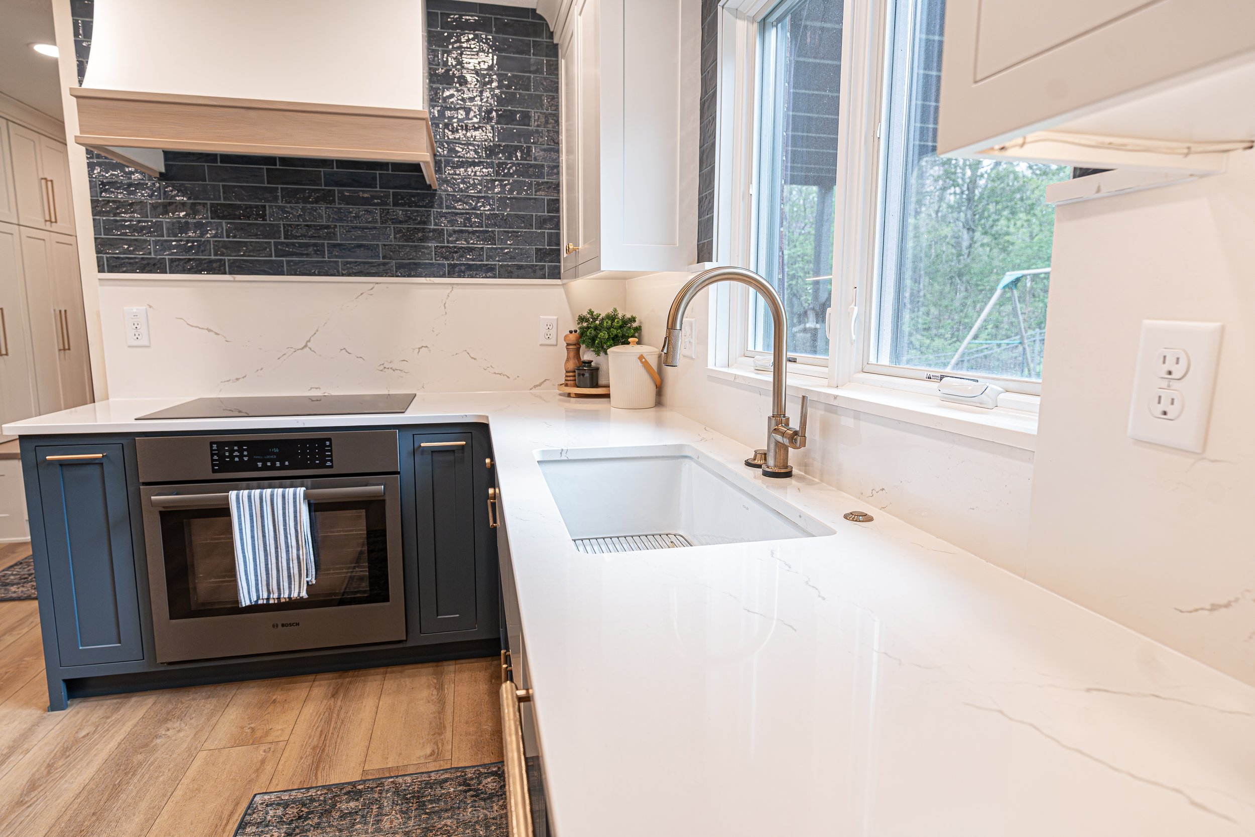 Apron-front farmhouse sink with a brass faucet, quartz counters centered under a window above navy cabinetry in a Centerville kitchen.