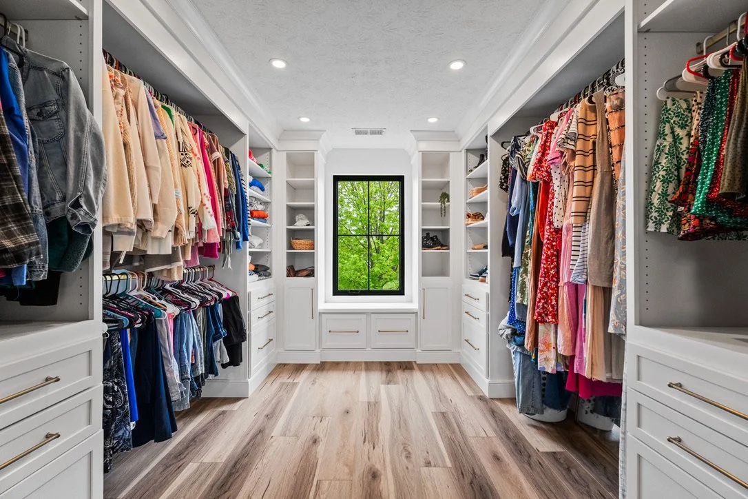 Walk-in closet with white built-in cabinetry, open hanging storage, and a central window in a Brookville, Ohio master suite.