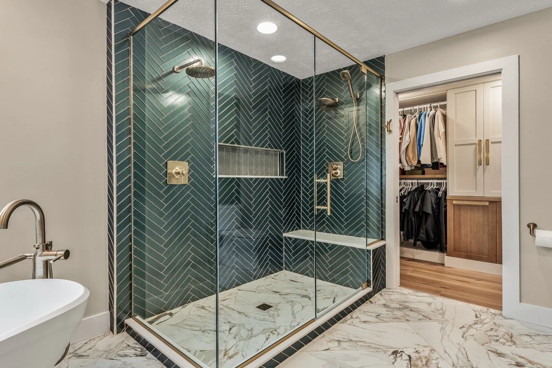 Spacious two-person glass shower with green herringbone tile, gold fixtures, a custom niche, and marble flooring in a Xenia, Ohio master bathroom