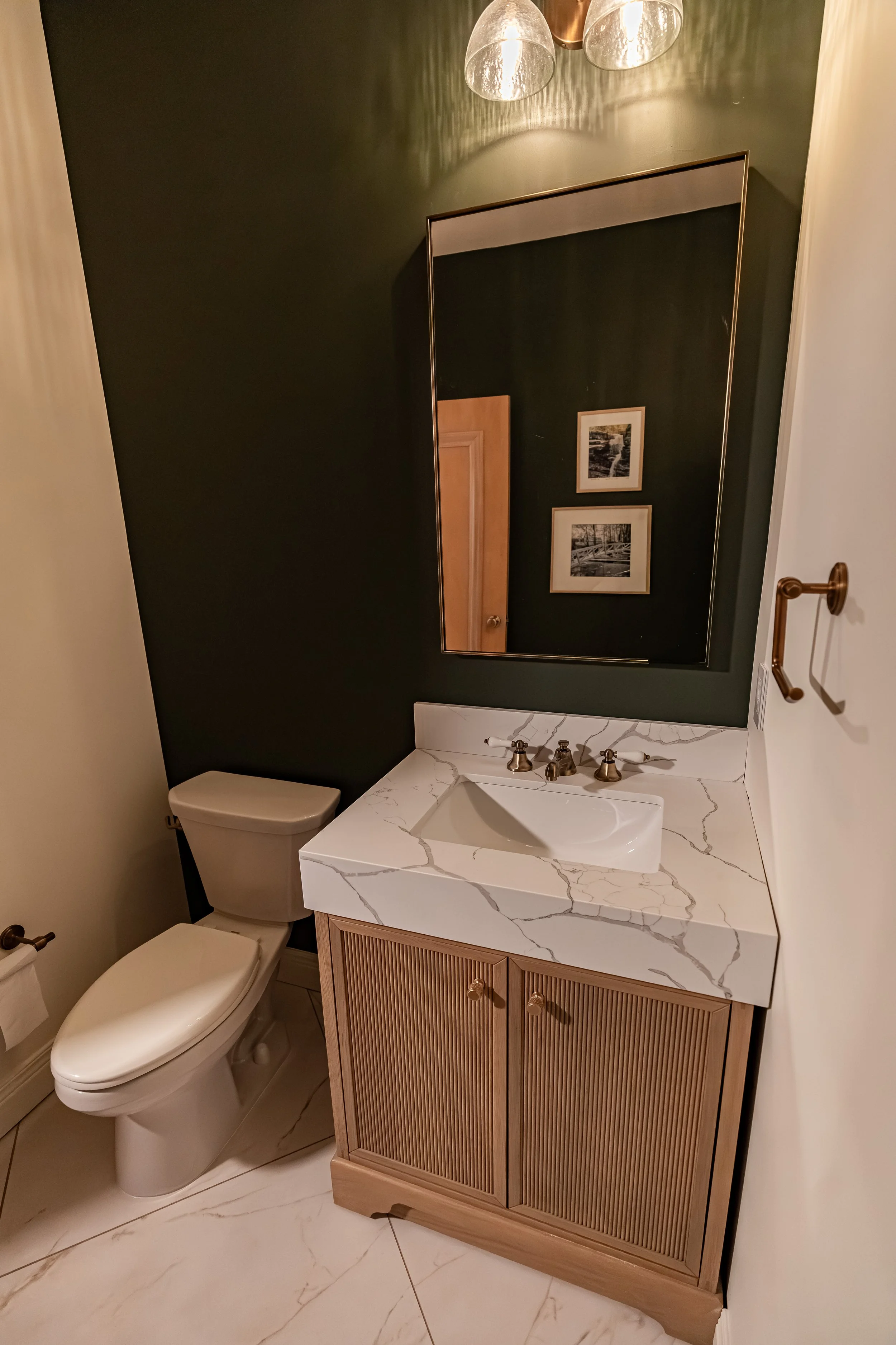 Powder room featuring a wood vanity, framed mirror, and marble-look tile flooring against deep green walls in a Bellbrook half bath.