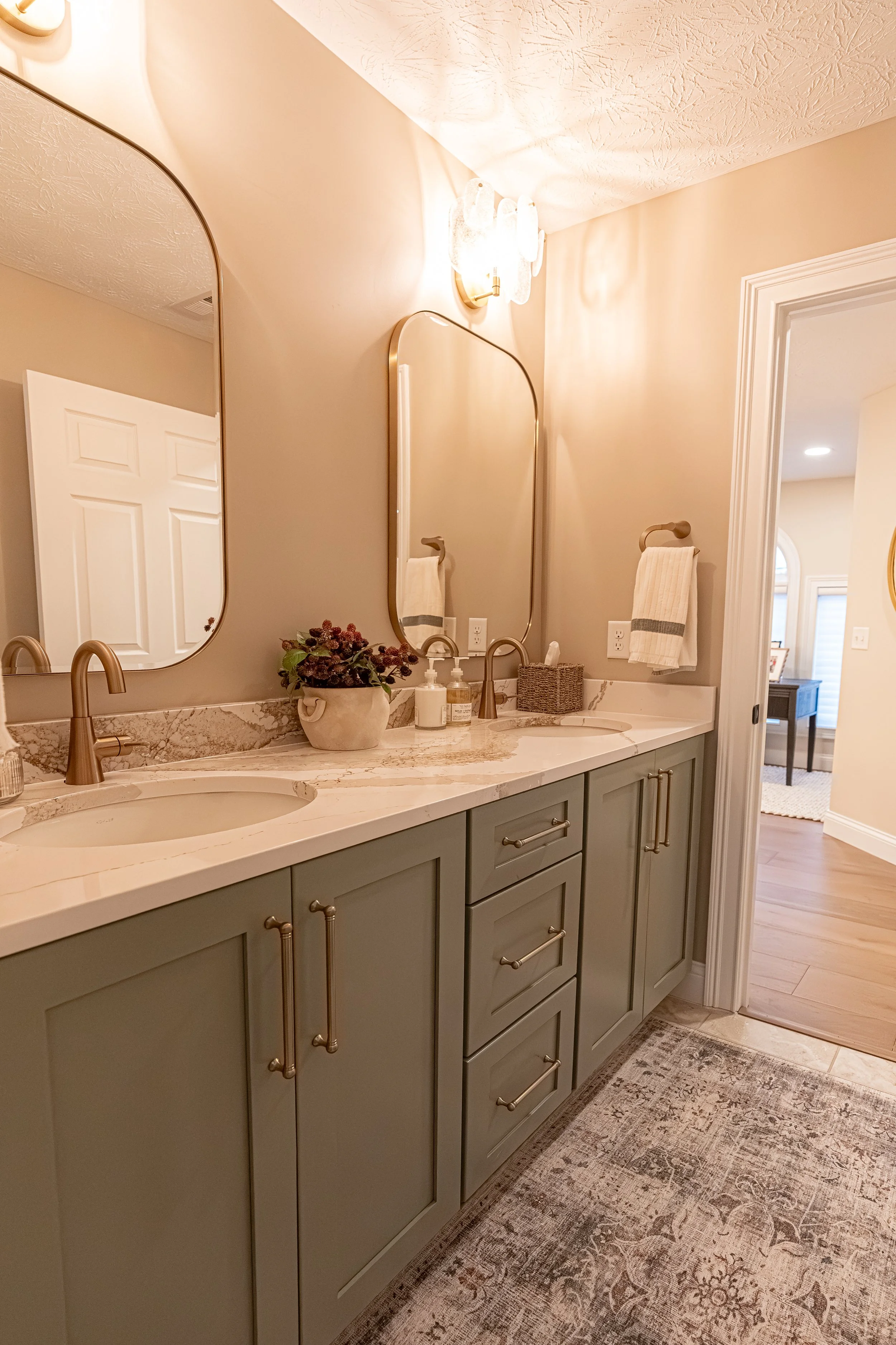 Guest bathroom with a green double vanity, quartz countertops, dual arched mirrors, brushed gold faucets and hardware, and a patterned runner in an Oakwood, Ohio home