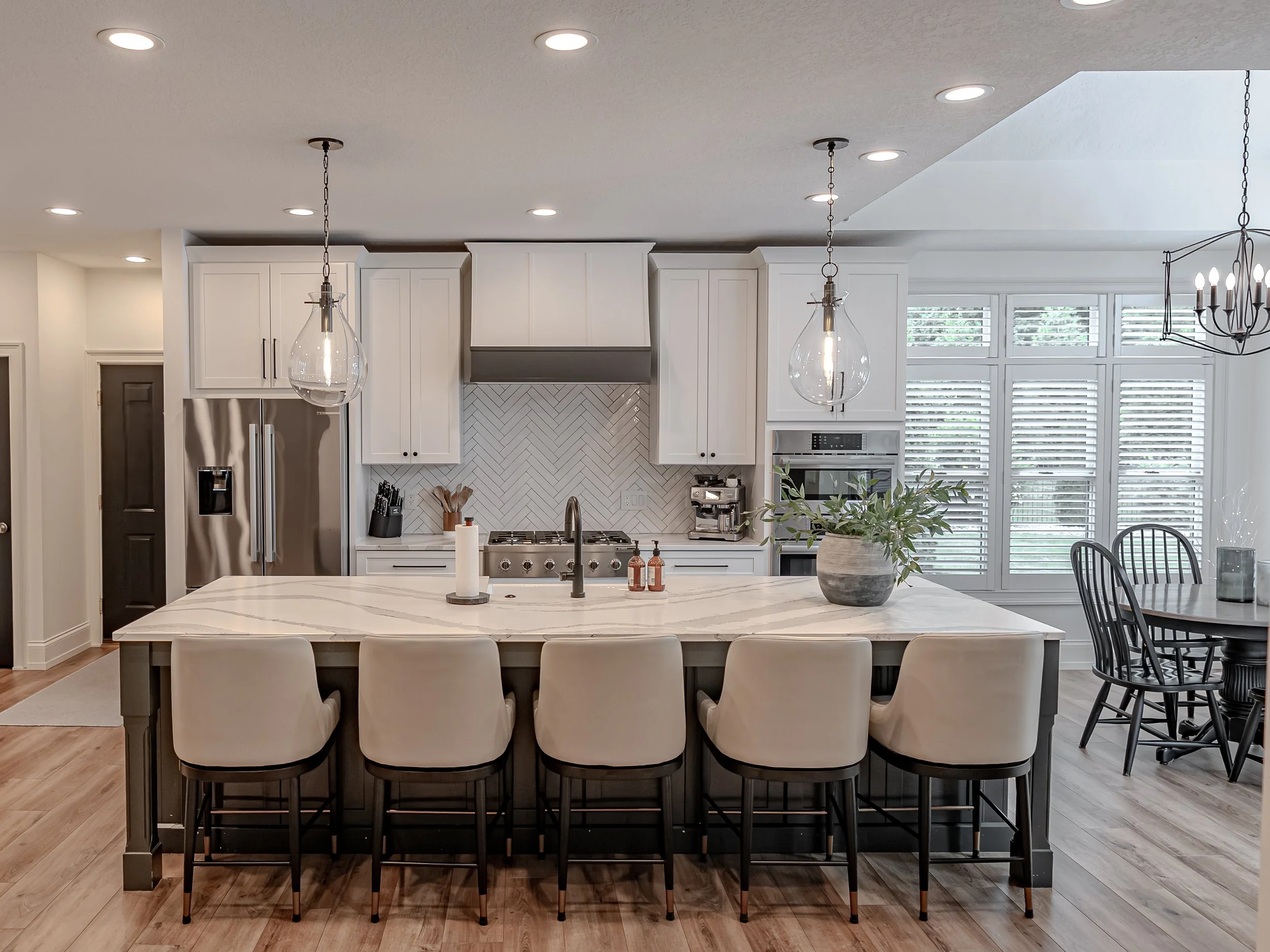 Modern kitchen with white cabinets, a large marble island, pendant lights, and large windows with blinds.