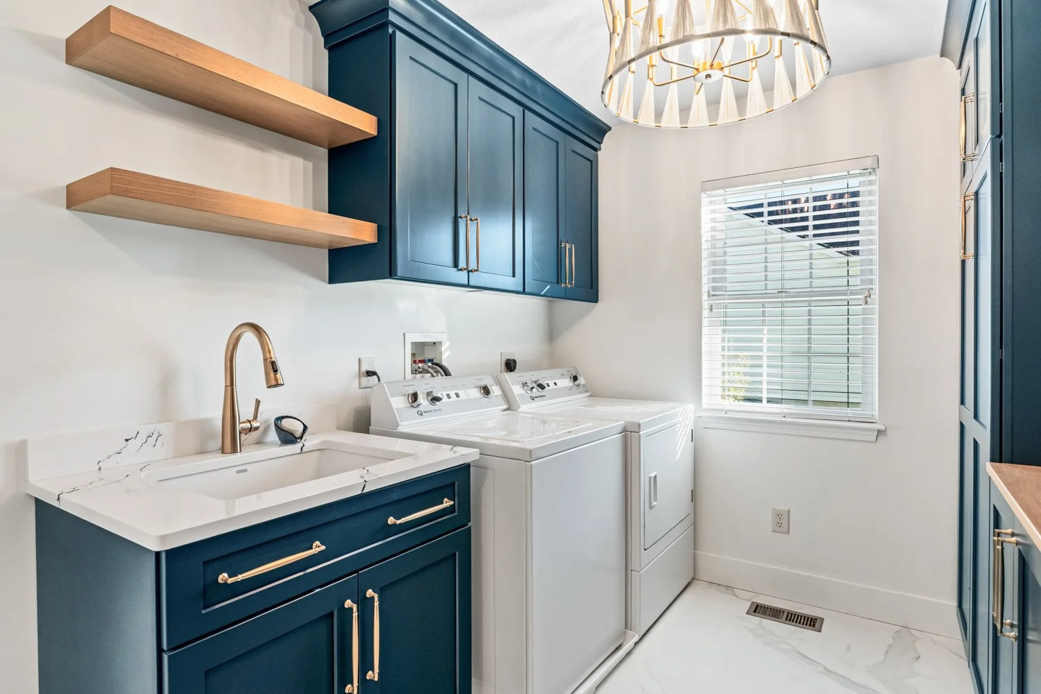 Laundry room with navy blue cabinetry, open wood shelving, brass fixtures, and a washer and dryer in a Beavercreek, Ohio main-level remodel.