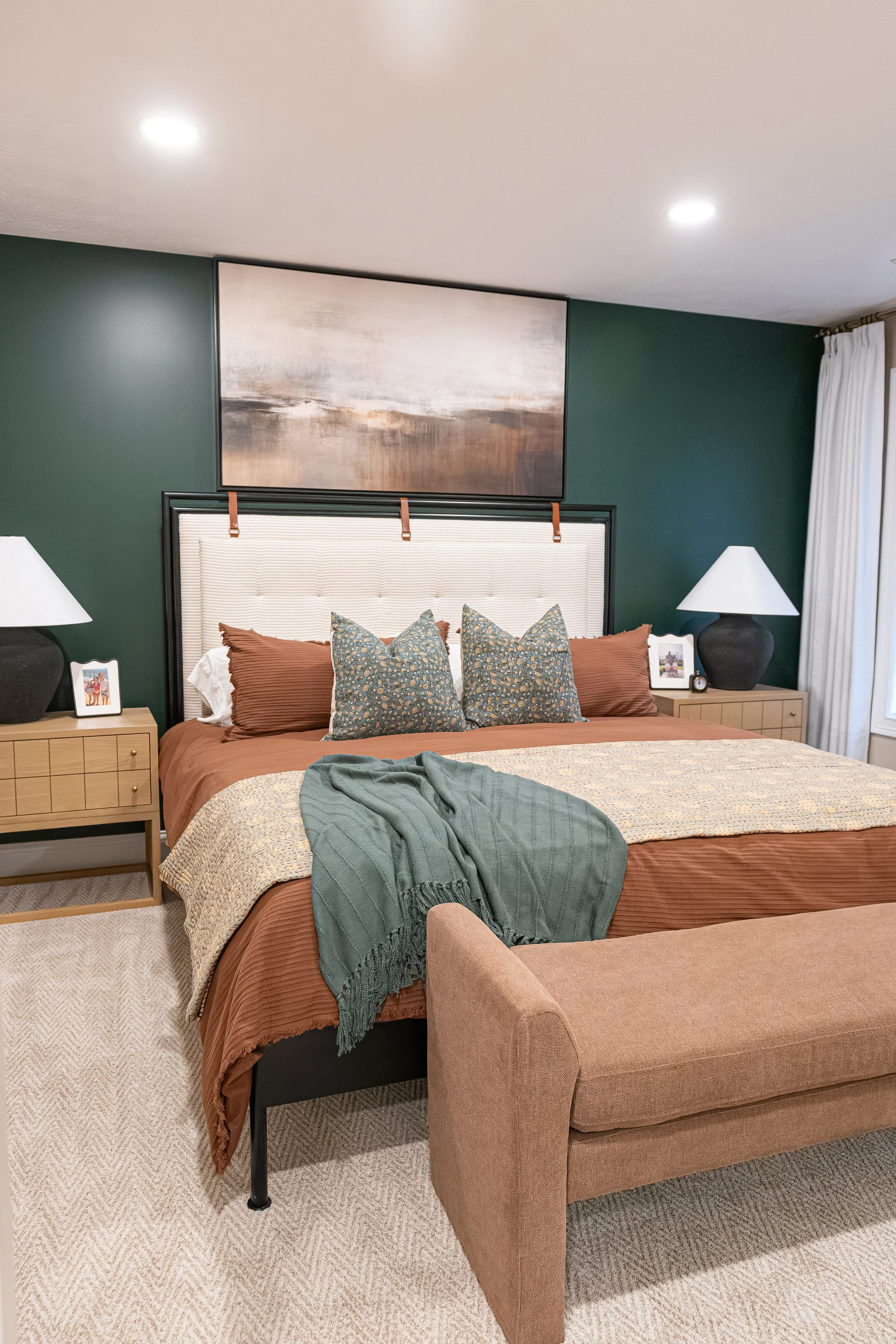 Guest bedroom with a blue-green accent wall, upholstered bed, rust-toned bedding, patterned accent pillows, and a landscape art piece in an Oakwood, Ohio home