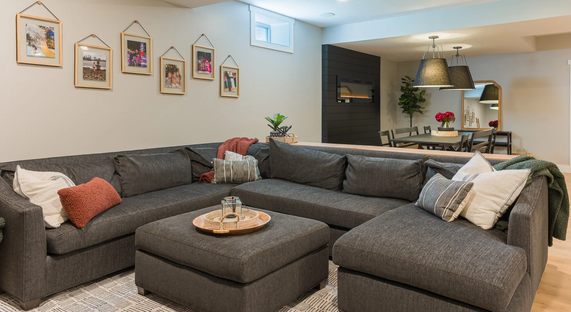Basement living area with a gray sectional, gallery wall, and dining space beyond in Beavercreek, Ohio