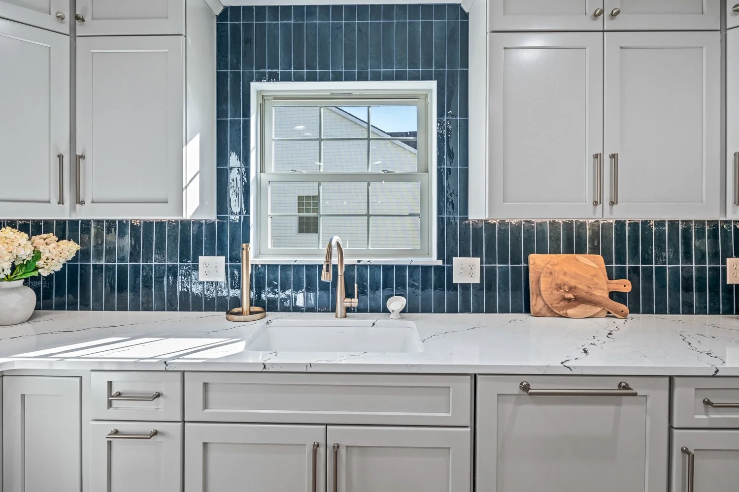 Kitchen sink with a brass faucet beneath a window framed by blue tile and quartz counters in a Beavercreek, Ohio kitchen remodel.