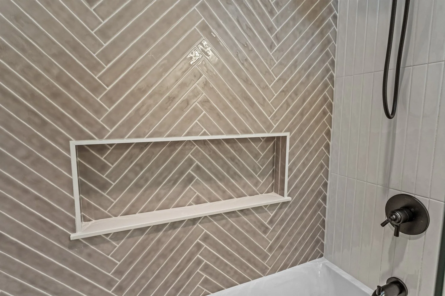 Gray herringbone tile shower surround with a long recessed shelf niche and brass wall hooks in a Centerville, Ohio basement bathroom.