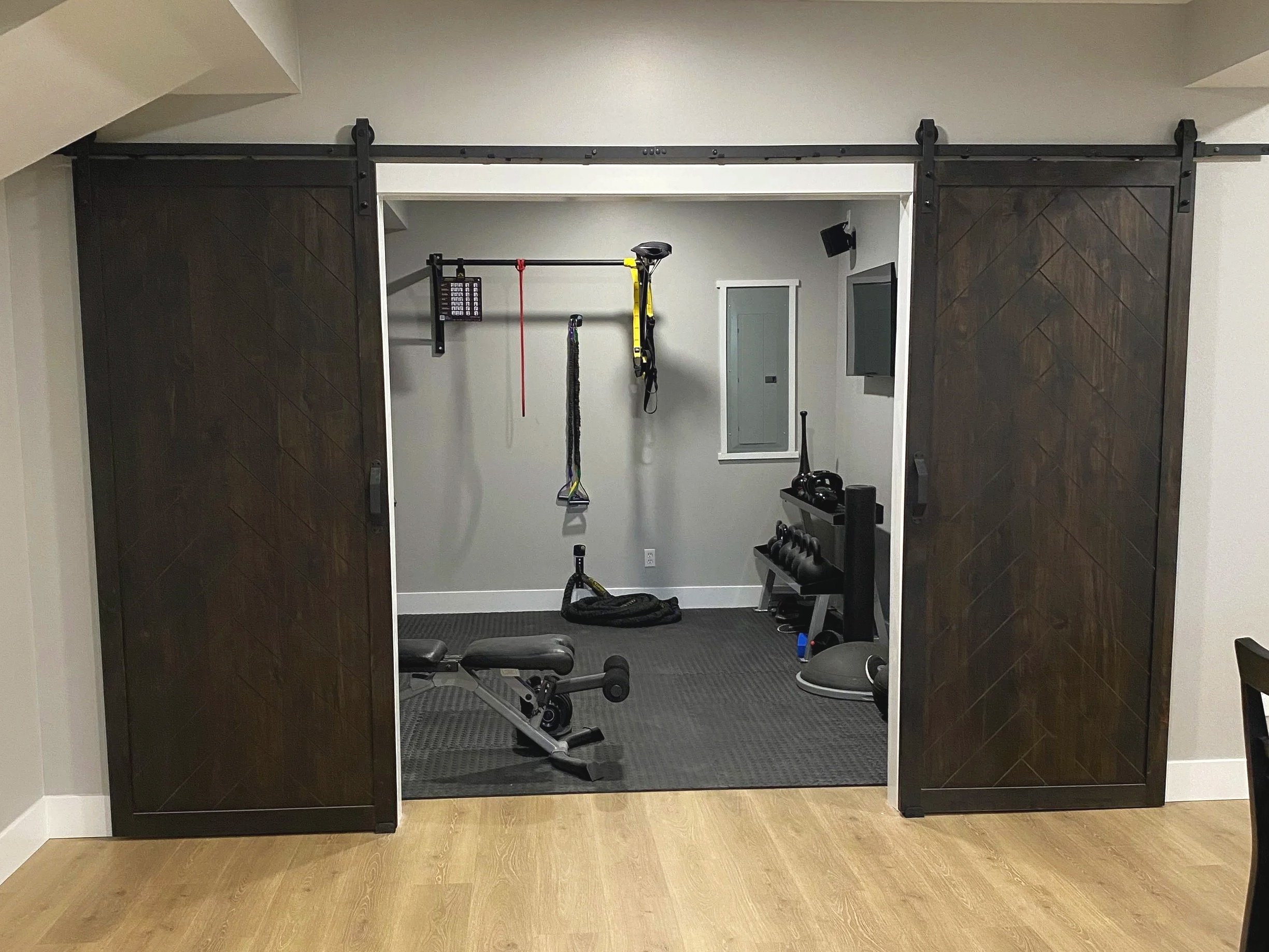 Home gym behind sliding barn doors in a finished basement renovation in Beavercreek, Ohio