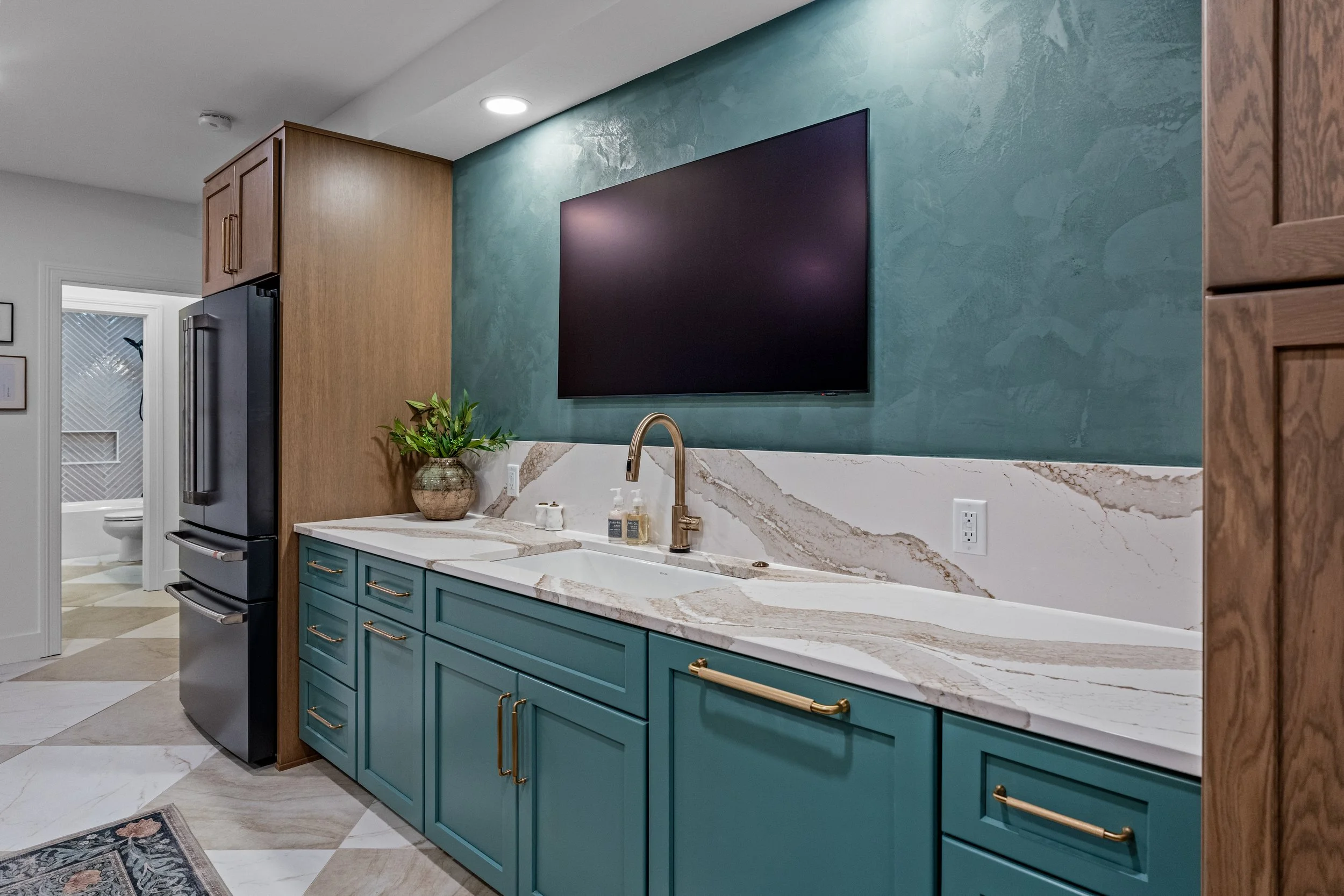 Finished basement bar and kitchen in Centerville, Ohio with teal cabinetry, a marble countertop, brass faucet, and wood accents by White Oak Interiors