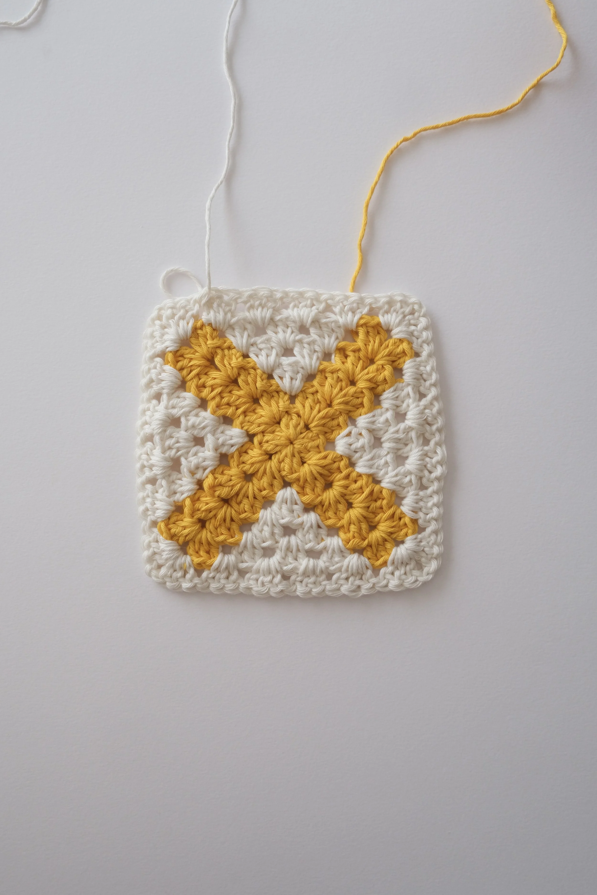 A crocheted square with a yellow cross pattern in the center, on a white background.