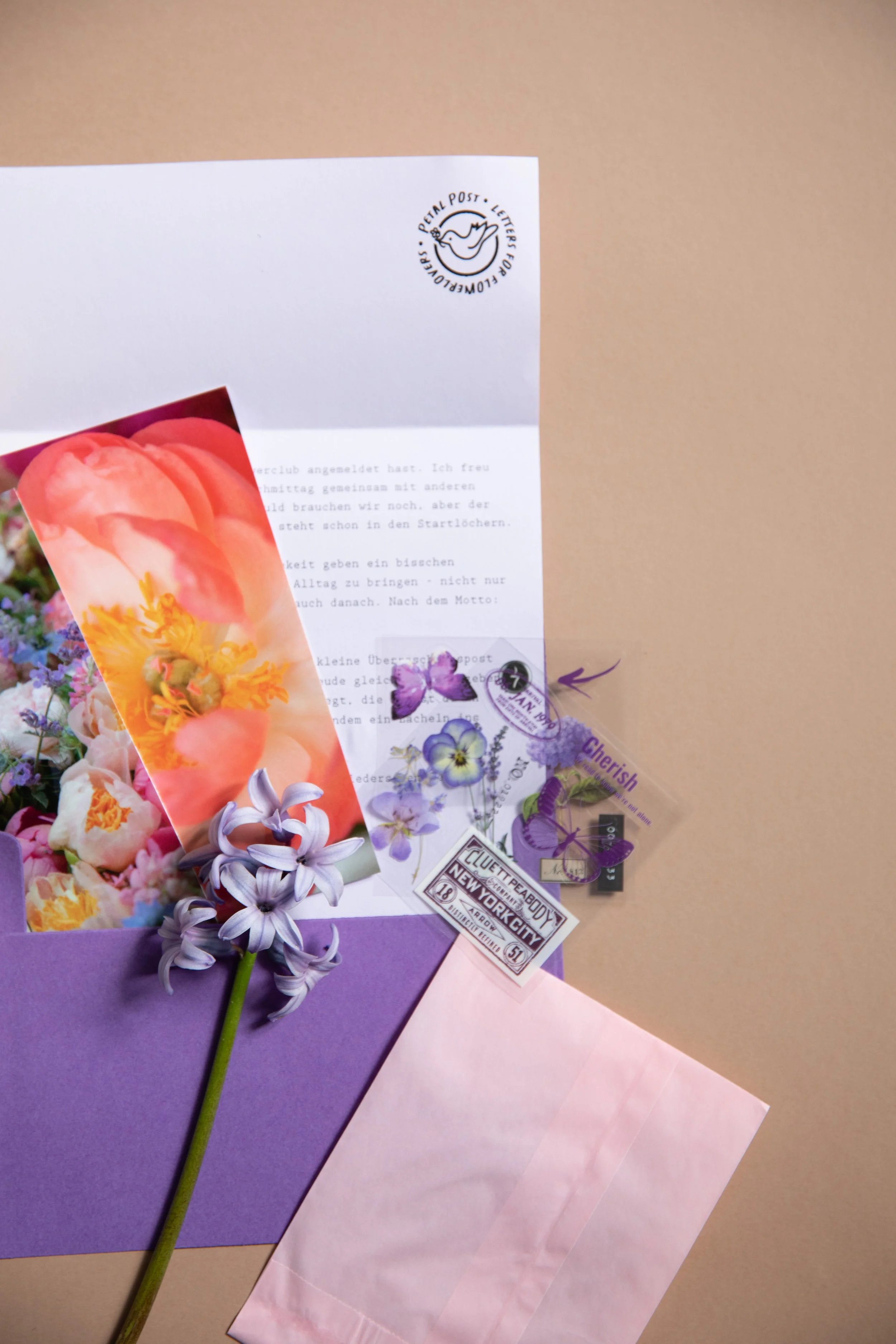 Ein Briefumschlag mit einem Stempel und verschiedenen Blumen, darunter eine rosa Tulpe, Lavendel und andere Blumen, auf bunten Papierbögen. Der Umschlag trägt einen Stempel, der einen Vogel und den Text 'PETERAL POST - LETTERS FOR FLOWER' zeigt.