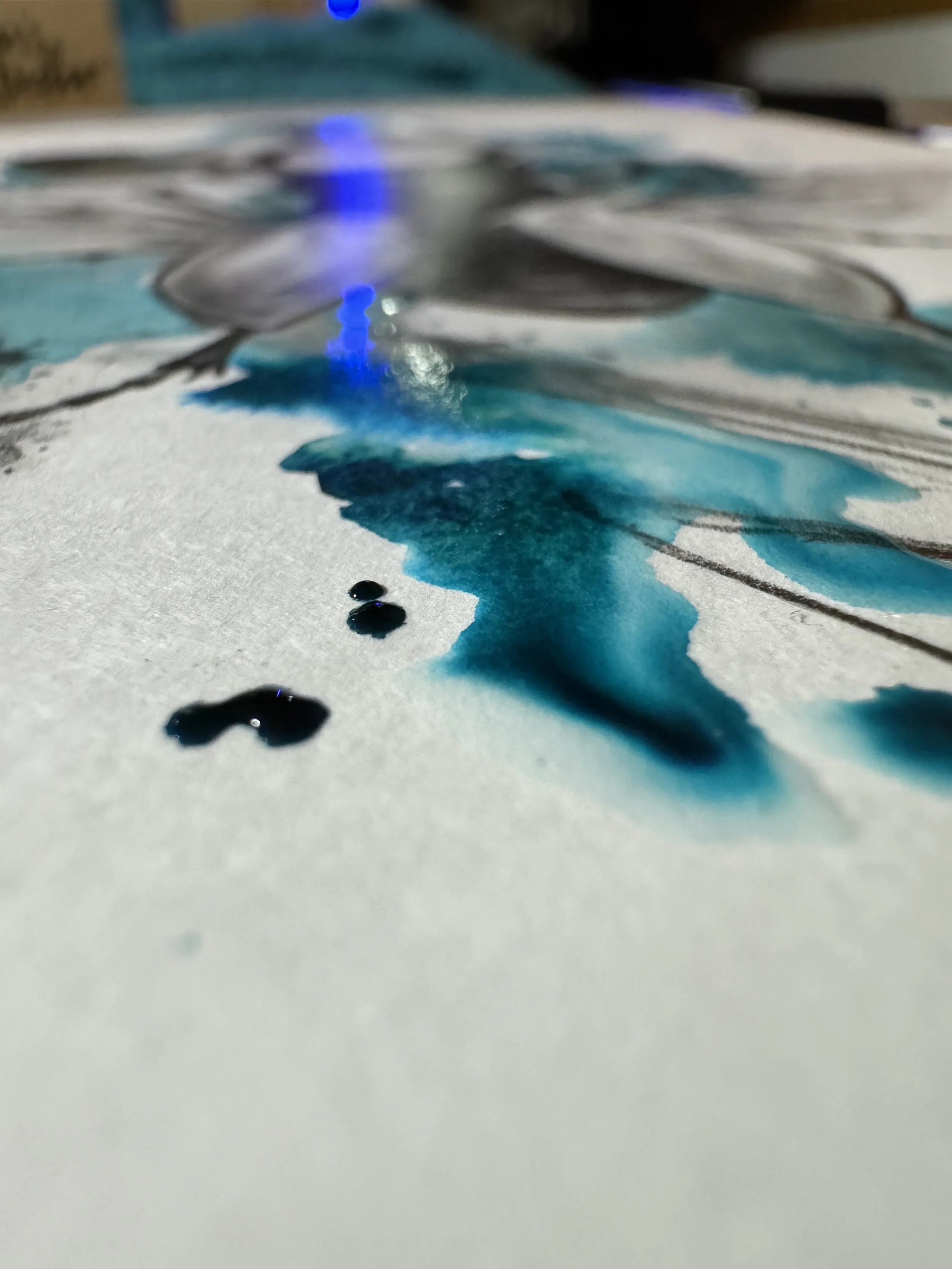 Close-up of blue and black ink spills on white paper, with blurred background.