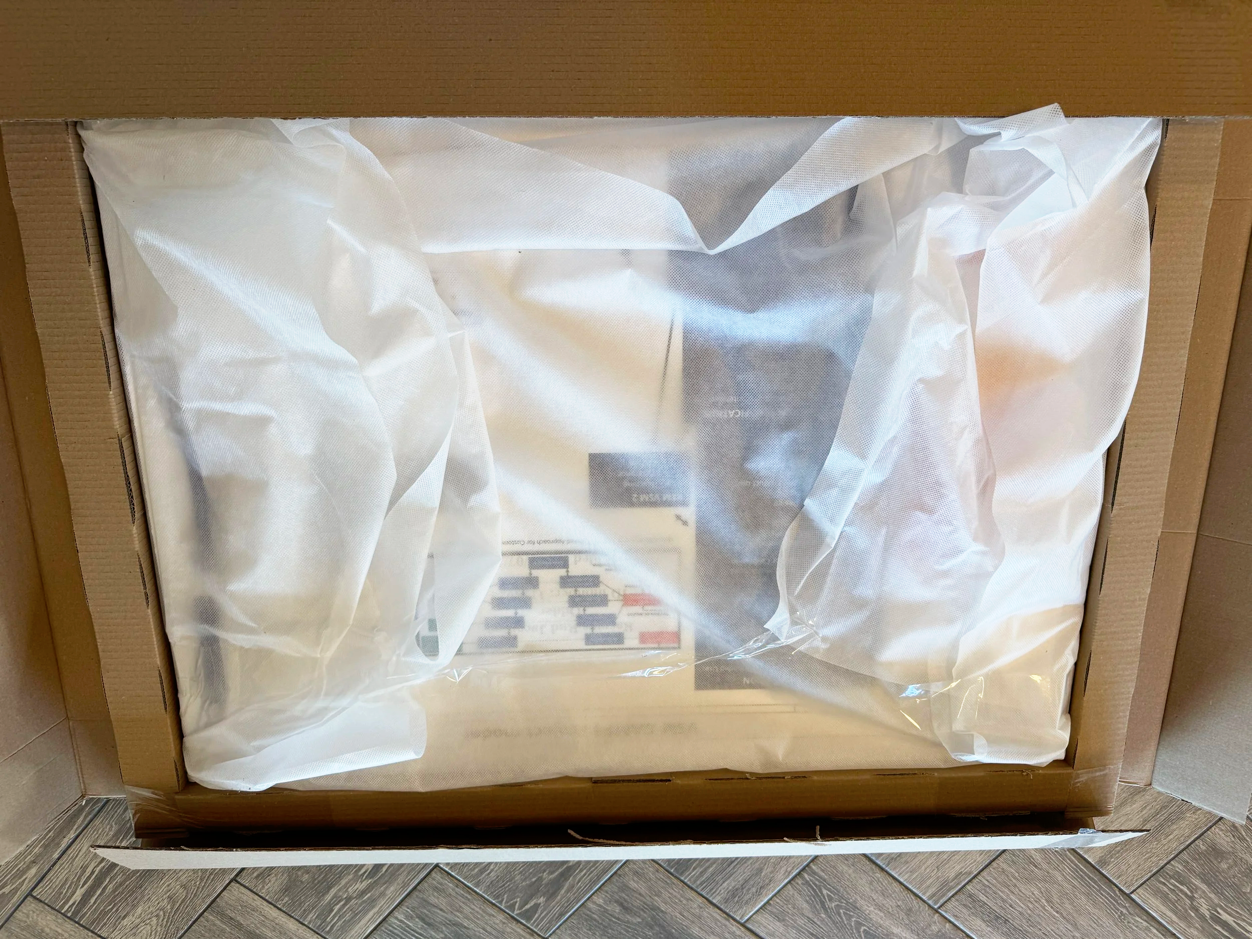 Open cardboard box with white paper padding inside, placed on a gray tiled floor.