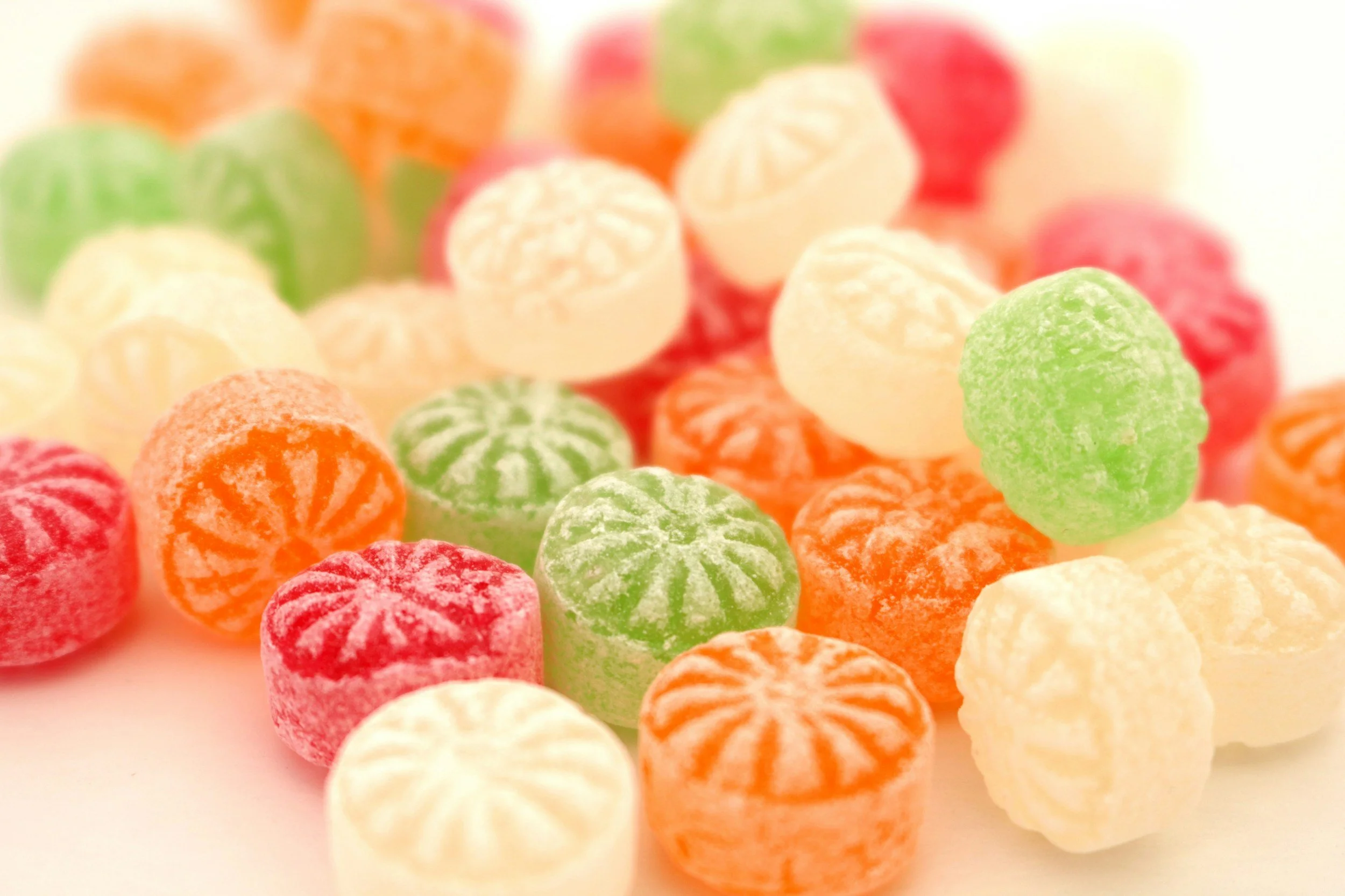 Colorful candies in various pastel shades scattered on a plain white surface.