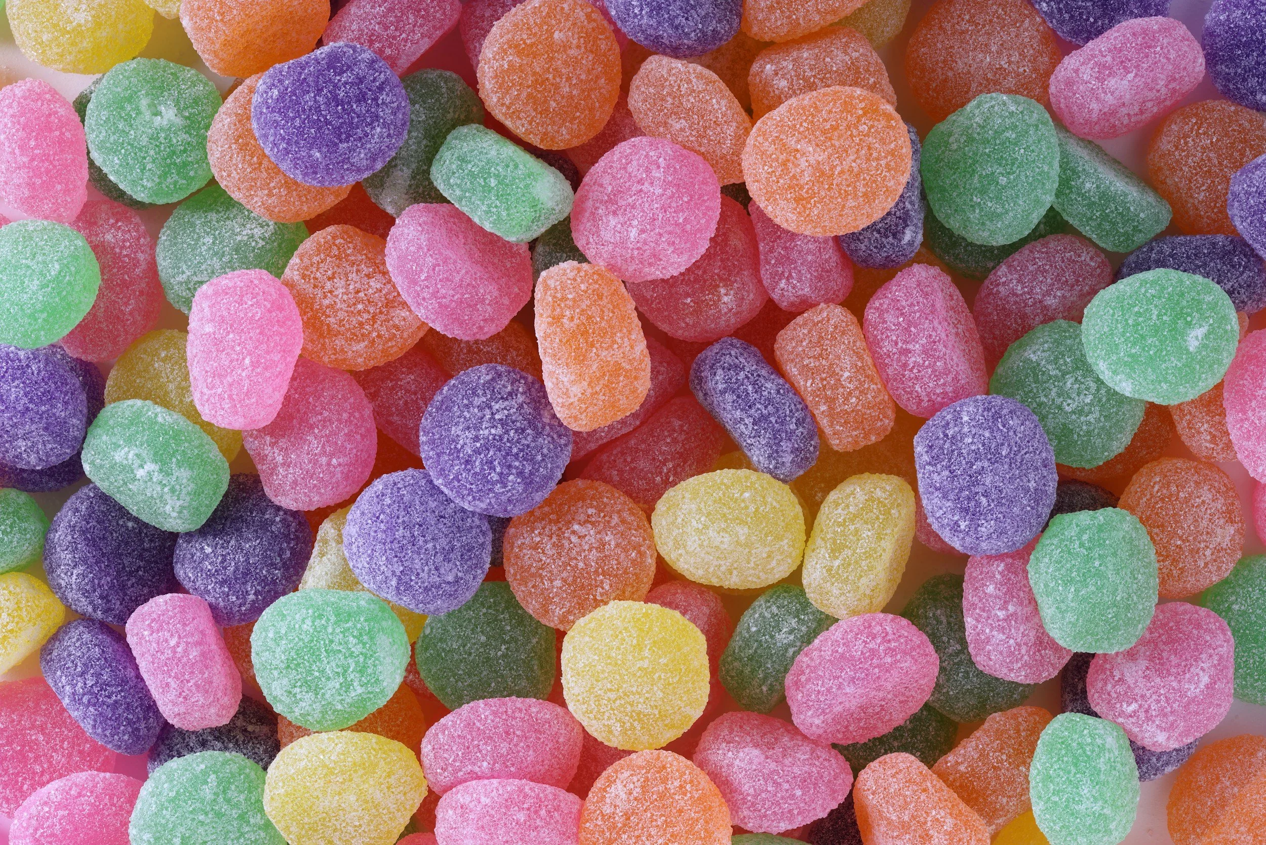 Close-up of multicolored sugar-coated gummy candies in shades of pink, green, purple, orange, and yellow.