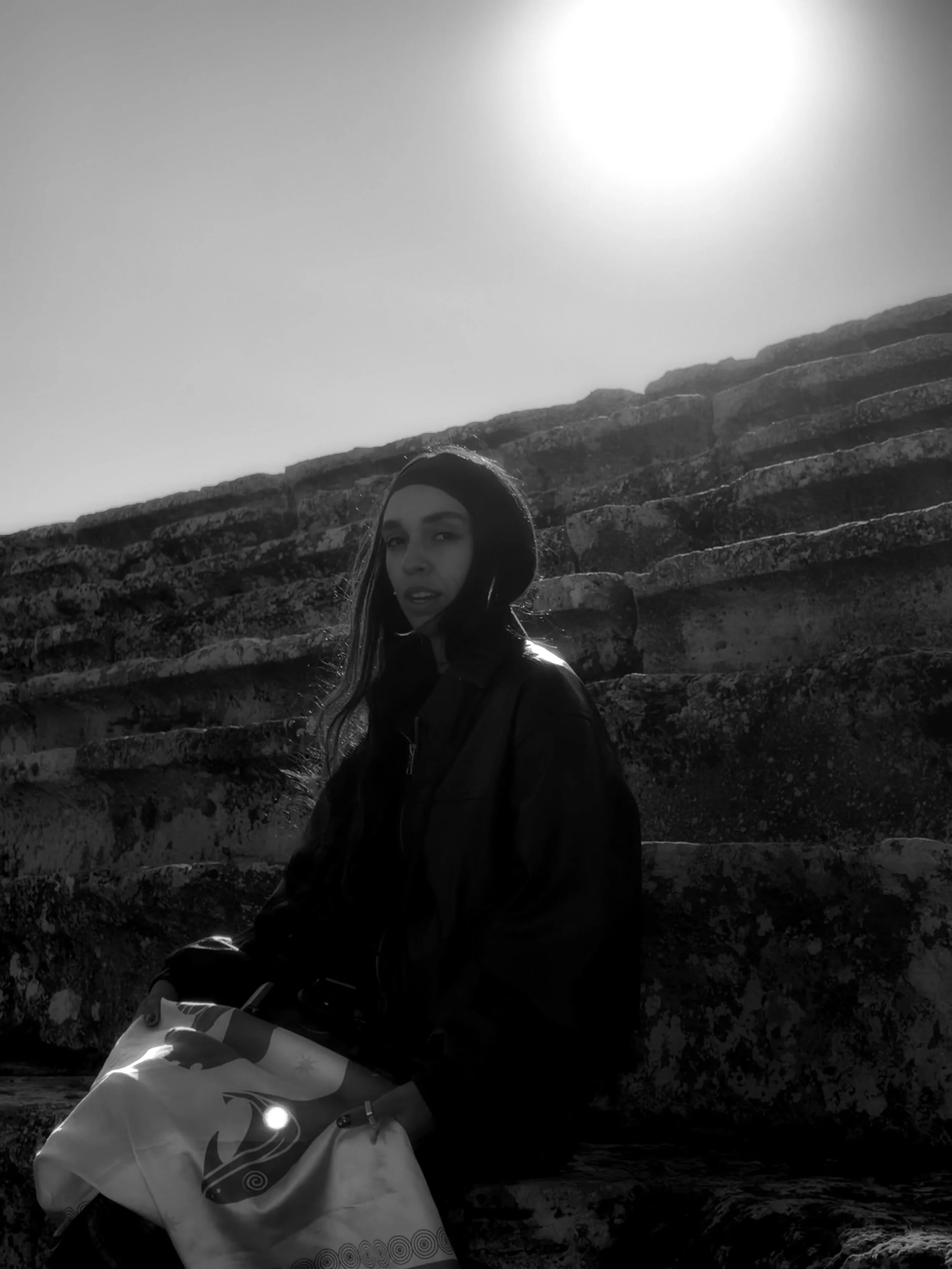 Una mujer sentada en unas gradas de piedra con el sol de fondo en un día soleado.