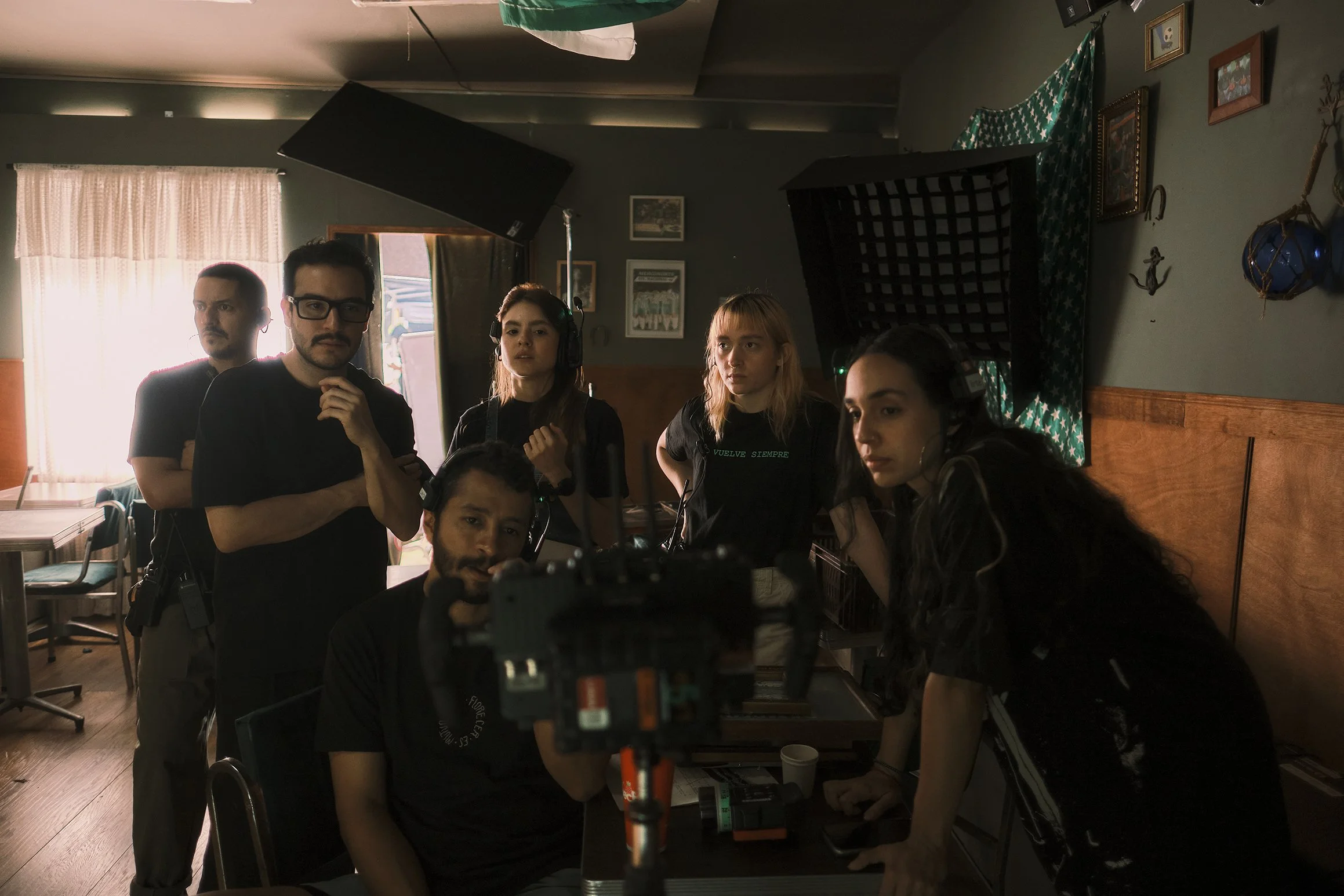 Equipo de filmación en un estudio, con cámara y luces, en un ambiente hogareño con paredes decoradas.