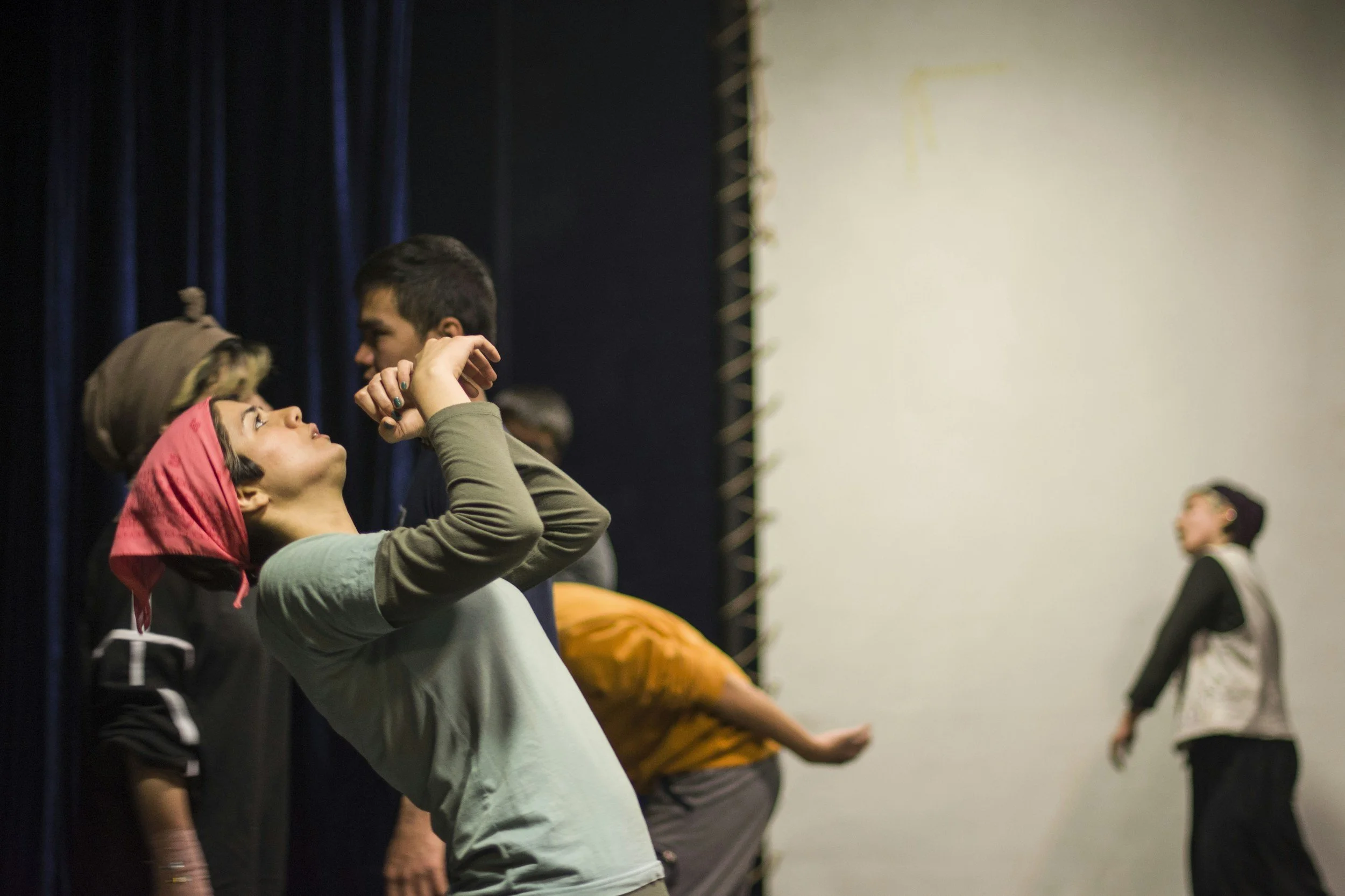 Twee jongeren iemand anders vermaakt zich op een podium met een donkere achtergrond en een witte muur.