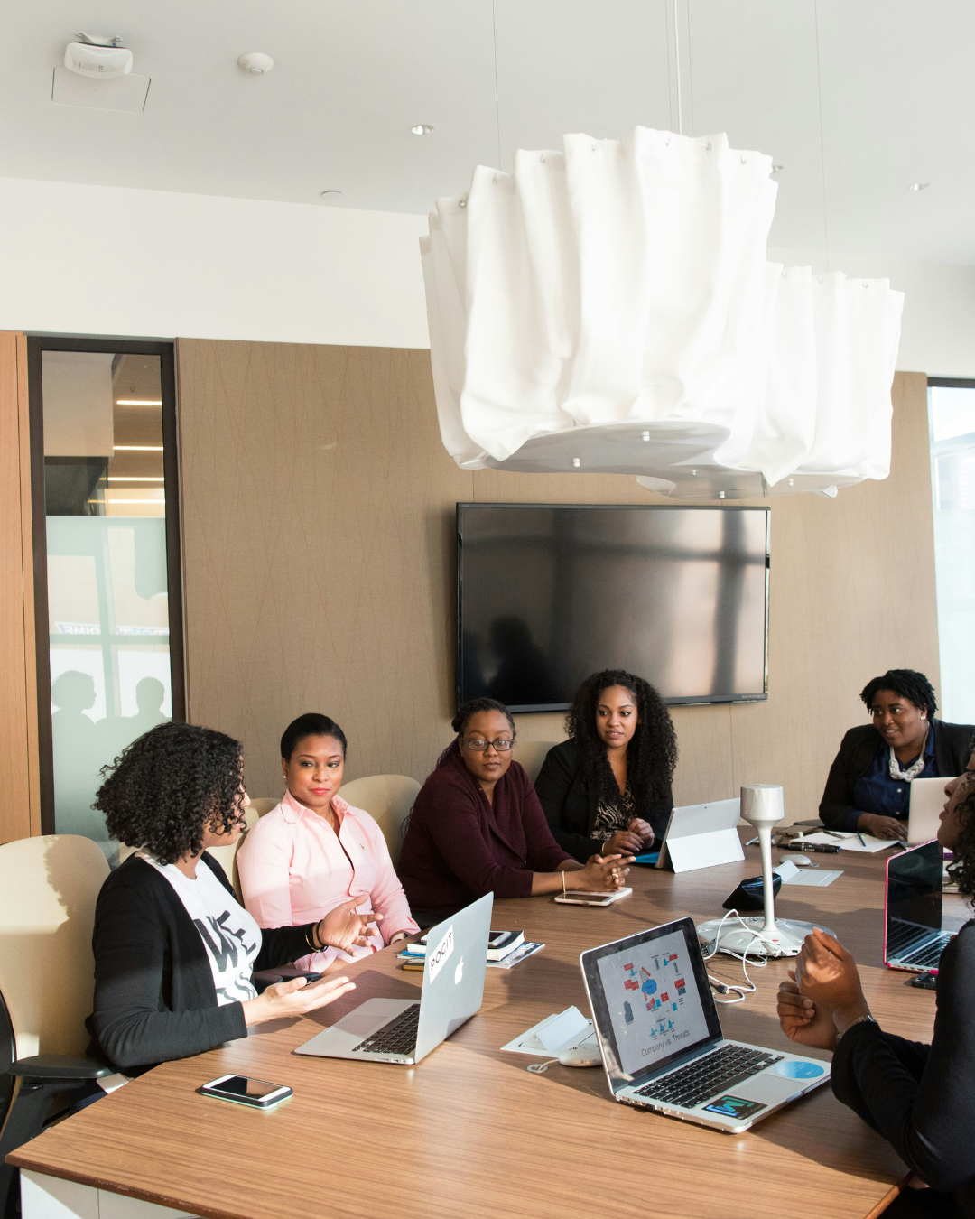 Group of women having a meeting in a modern conference room with laptops and tablets on the table.