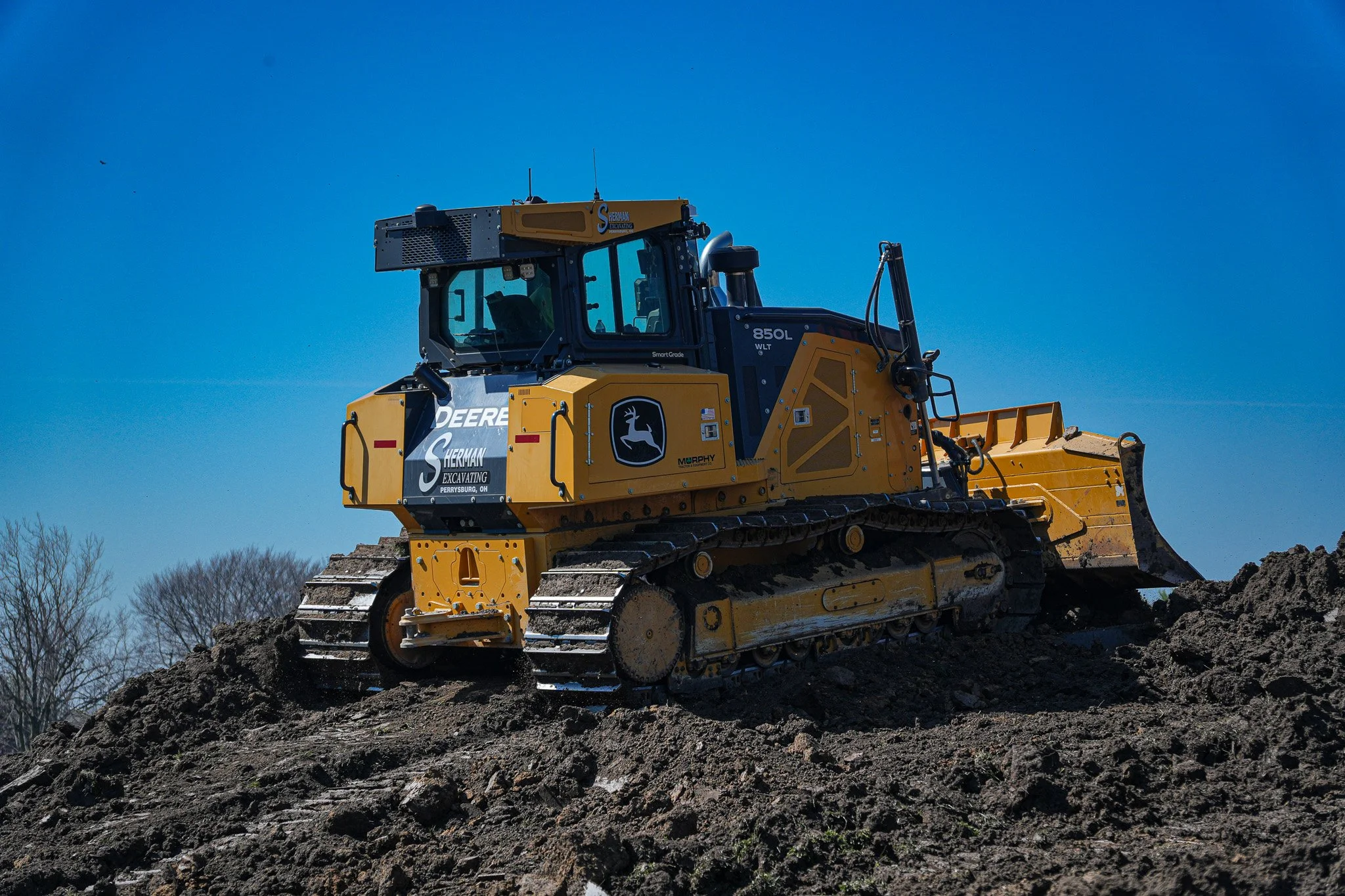 A large yellow bulldozer labeled Sherman Excavating on a mound of dirt under a clear blue sky.