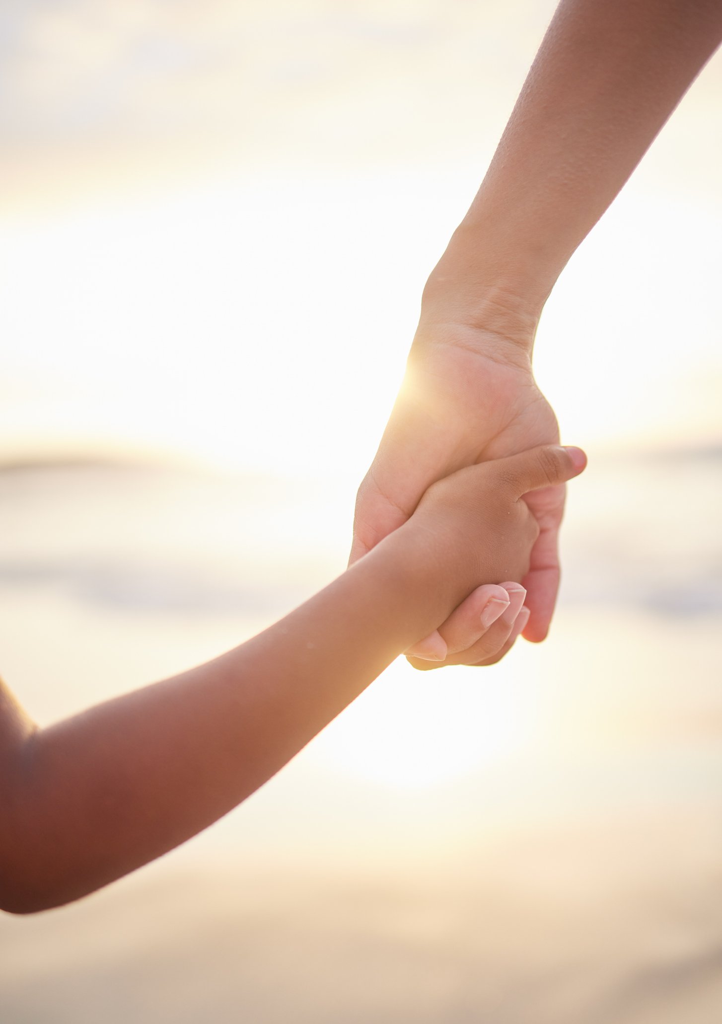 Close-up of an adult hand holding a child's hand against a blurred light background.