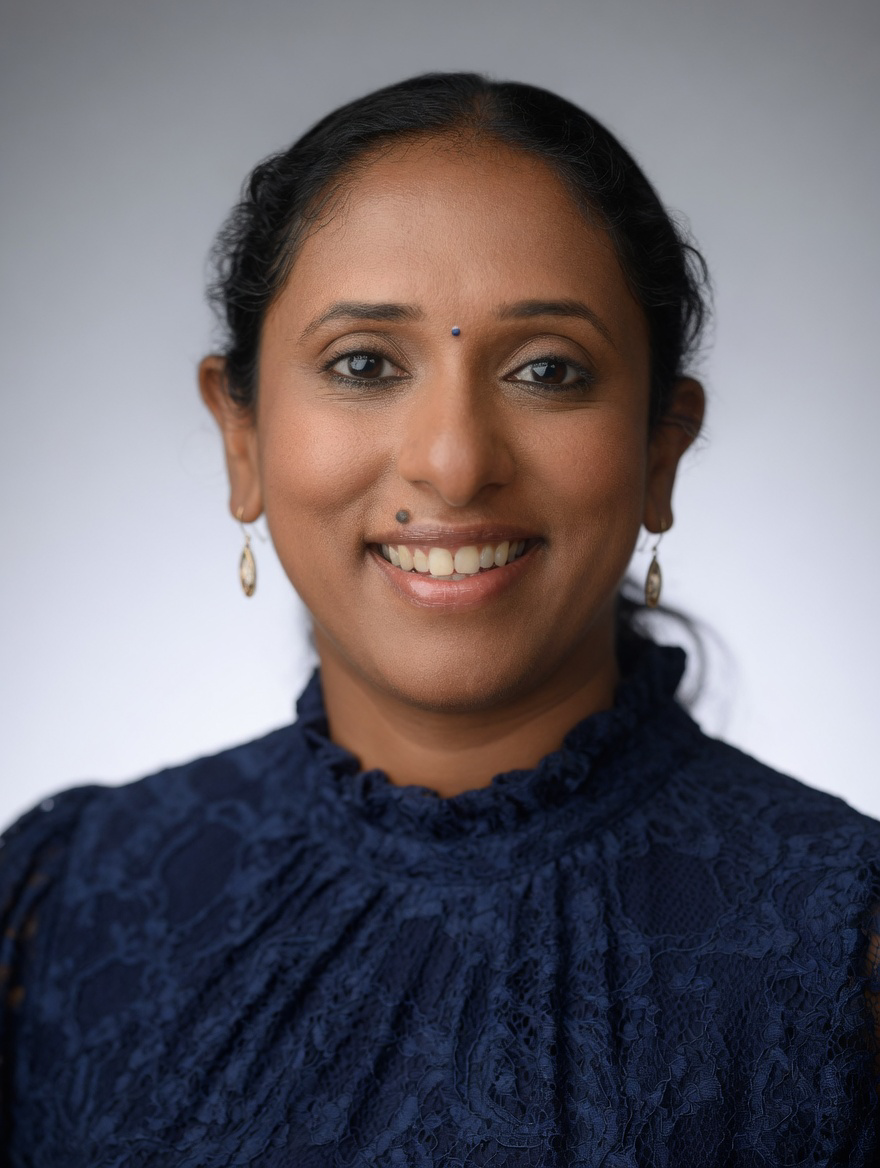 Close-up portrait of a smiling woman with dark hair, wearing earrings and a dark blue lace top.