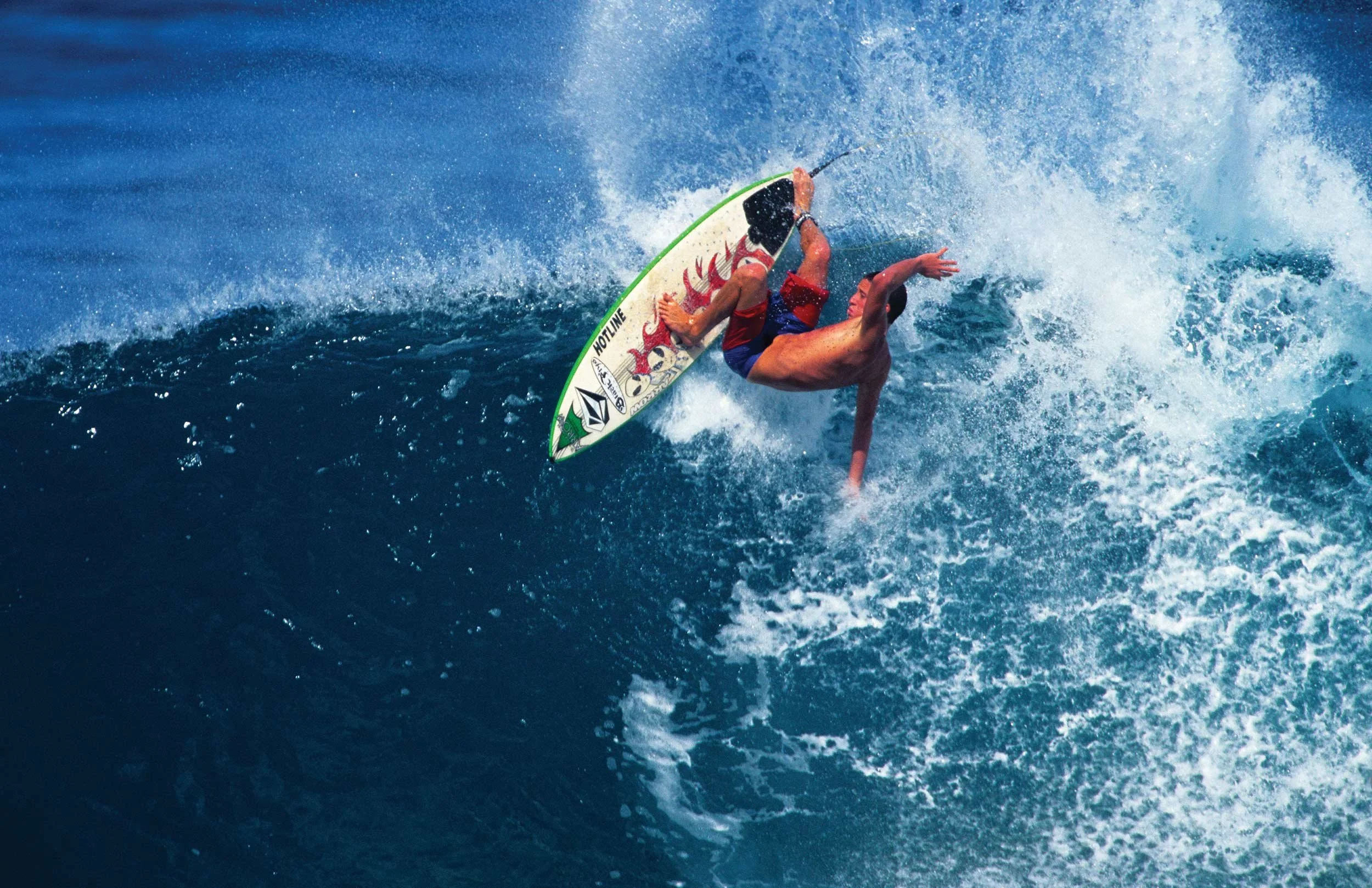 A person surfing on a wave in the ocean, wearing red and blue swim trunks, capturing a dynamic moment as they ride the wave.