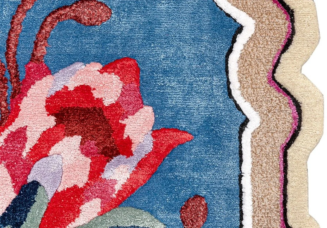 Close-up of a colorful embroidered rug with a floral pattern featuring red, pink, white, beige, black, and blue colors.