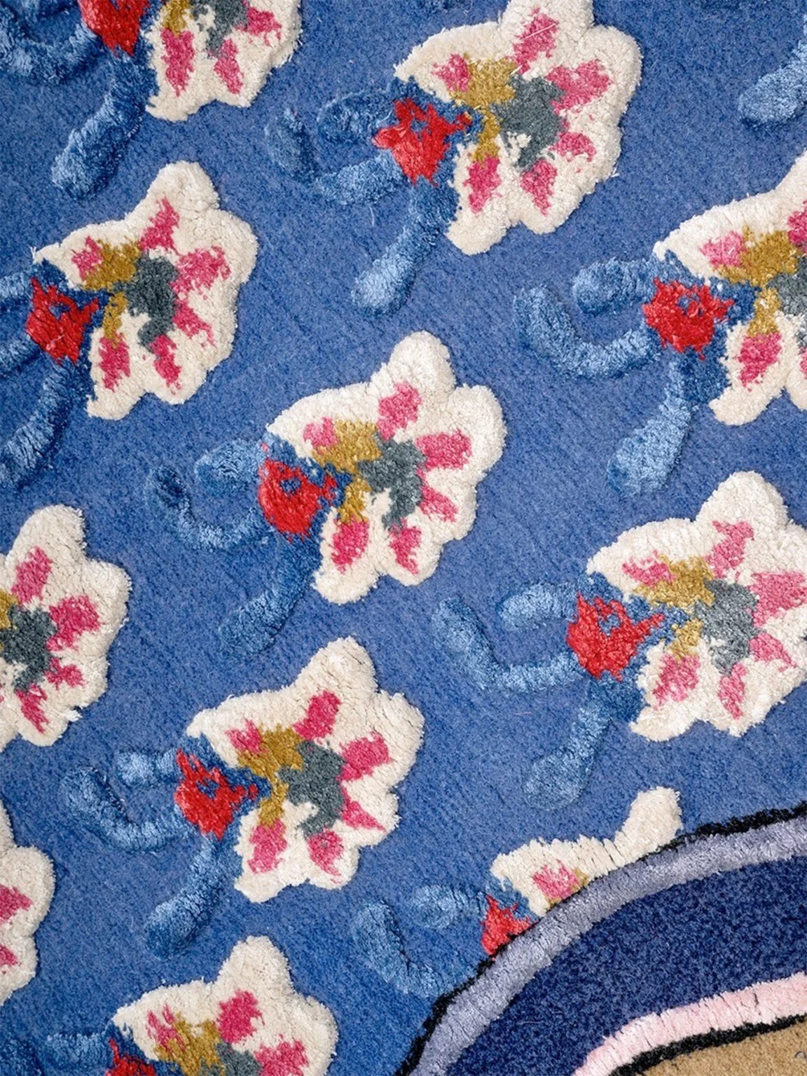 Close-up of a blue carpet with floral embroidery featuring white flowers with pink, red, gray, and gold accents.