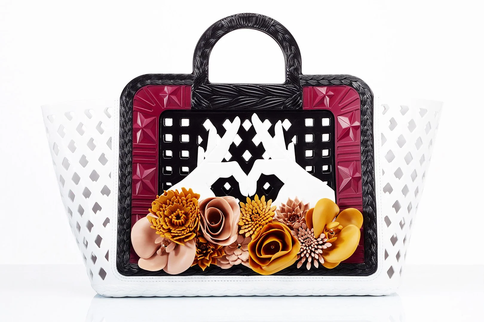 A decorative shopping basket with a black and red handle, white sides, and a black lid with floral and geometric cutouts, filled with yellow and beige paper flowers.