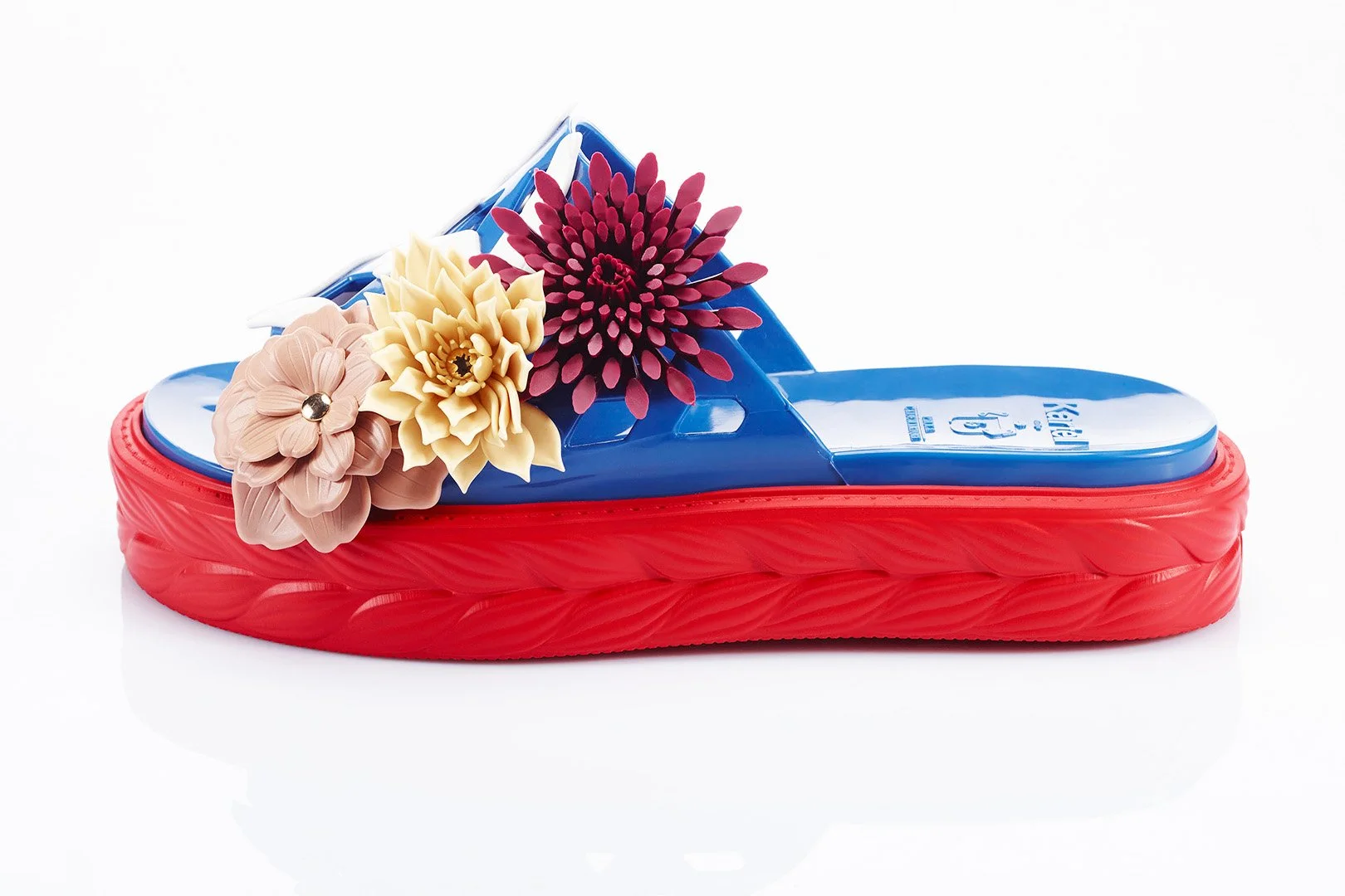 A colorful slide sandal decorated with pastel pink, yellow, and dark pink flowers on a red sole.