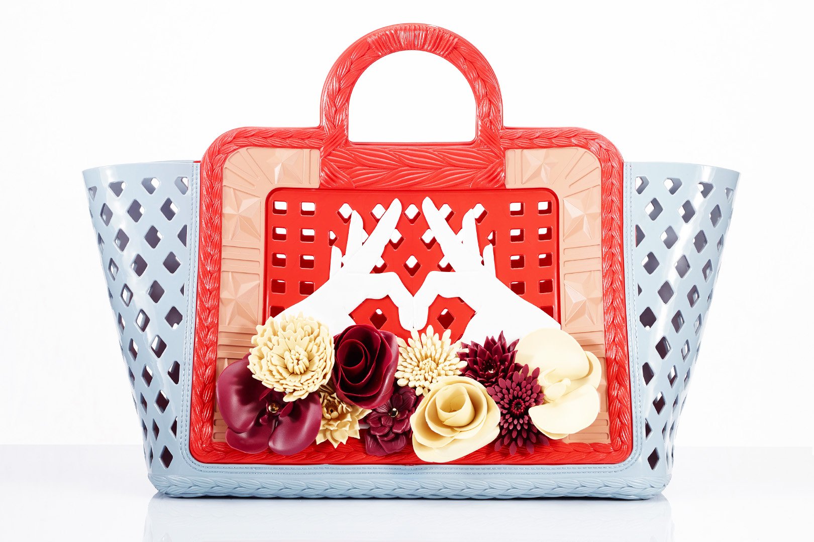 A colorful handbag with a floral arrangement and decorative cutout hands in front.