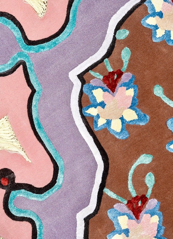 Close-up of a colorful, detailed embroidery or textile pattern with floral and abstract designs in pink, purple, brown, blue, and black colors.