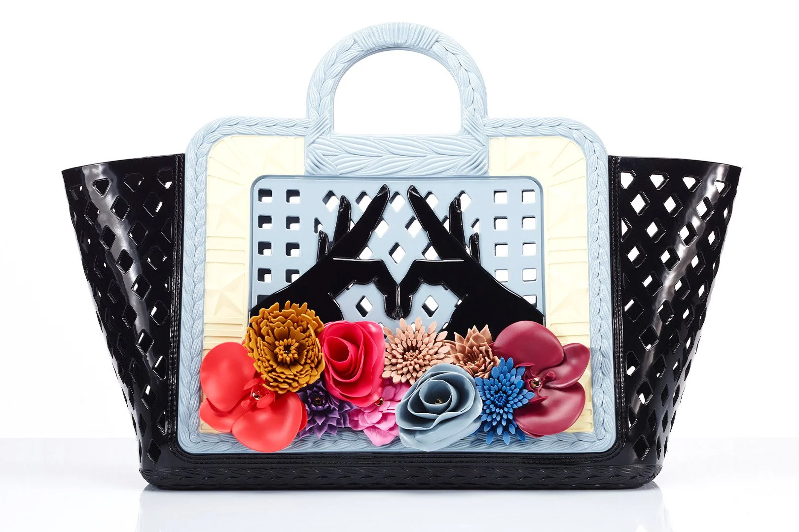 A black handbag with a lattice design containing colorful paper flowers and a clasp shaped like two hands forming a triangle.
