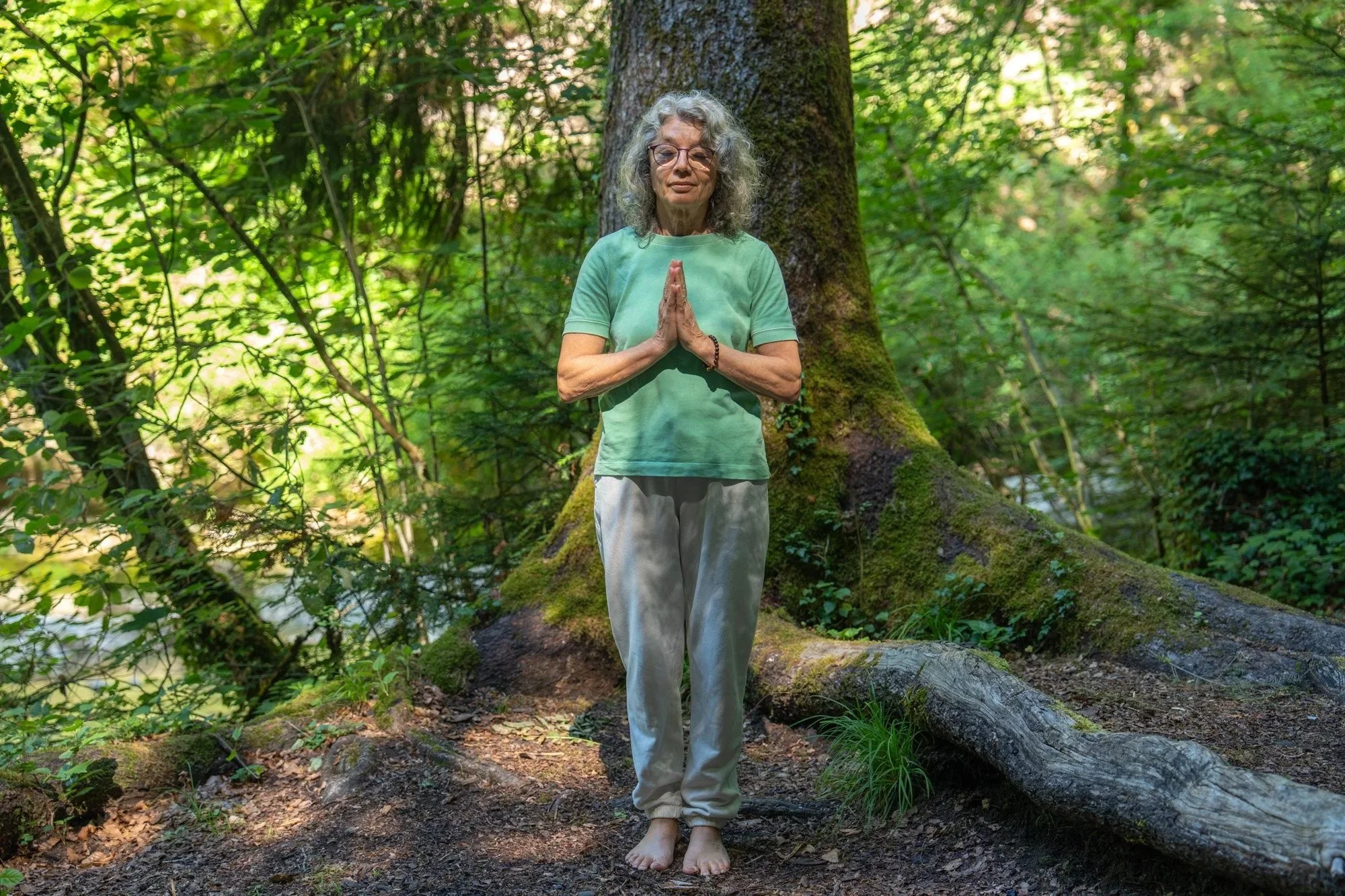 Femme âgée méditant pieds nus dans une forêt dense