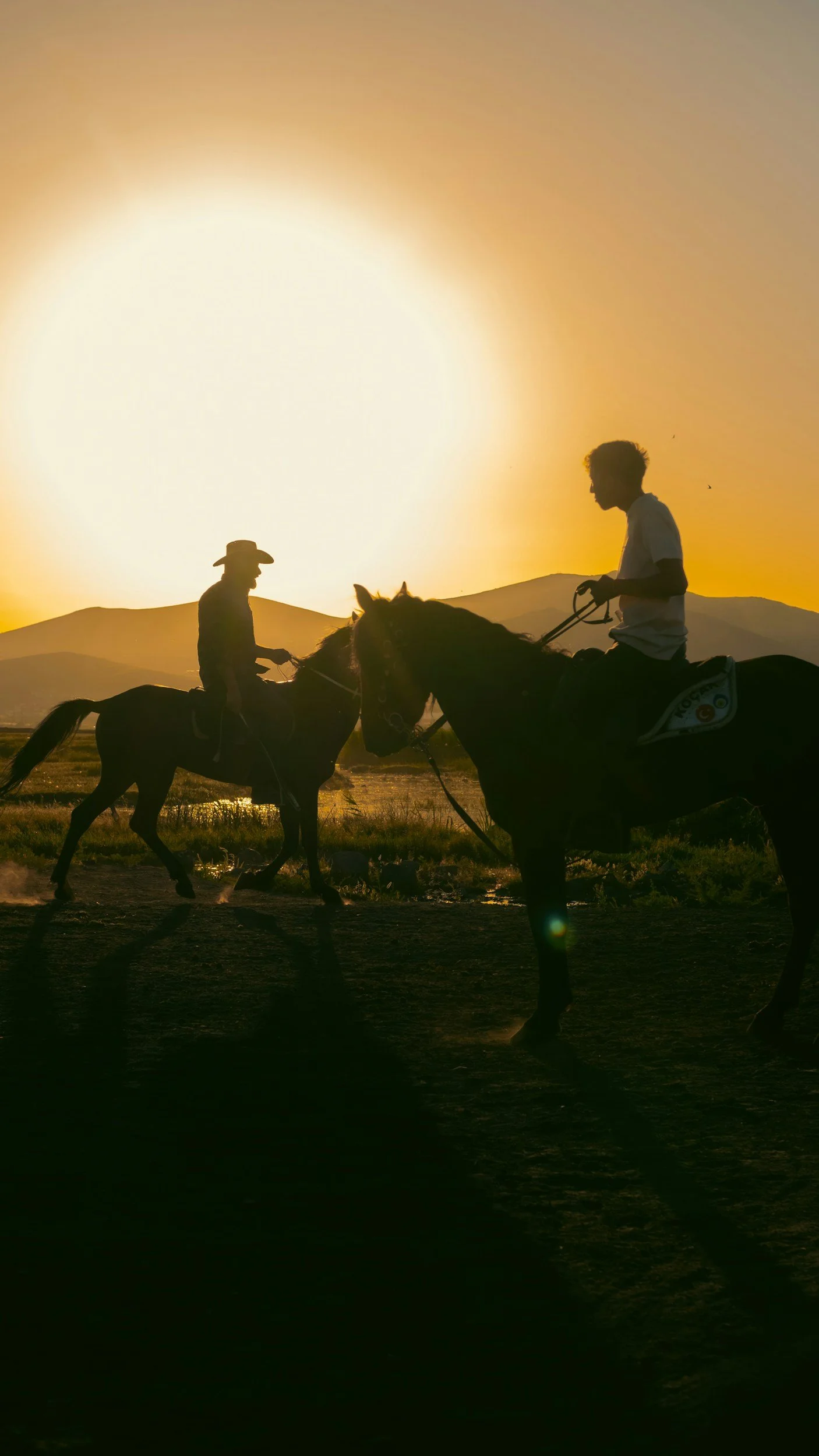 Silhouettes of two people riding horses at sunset with mountains in the background.