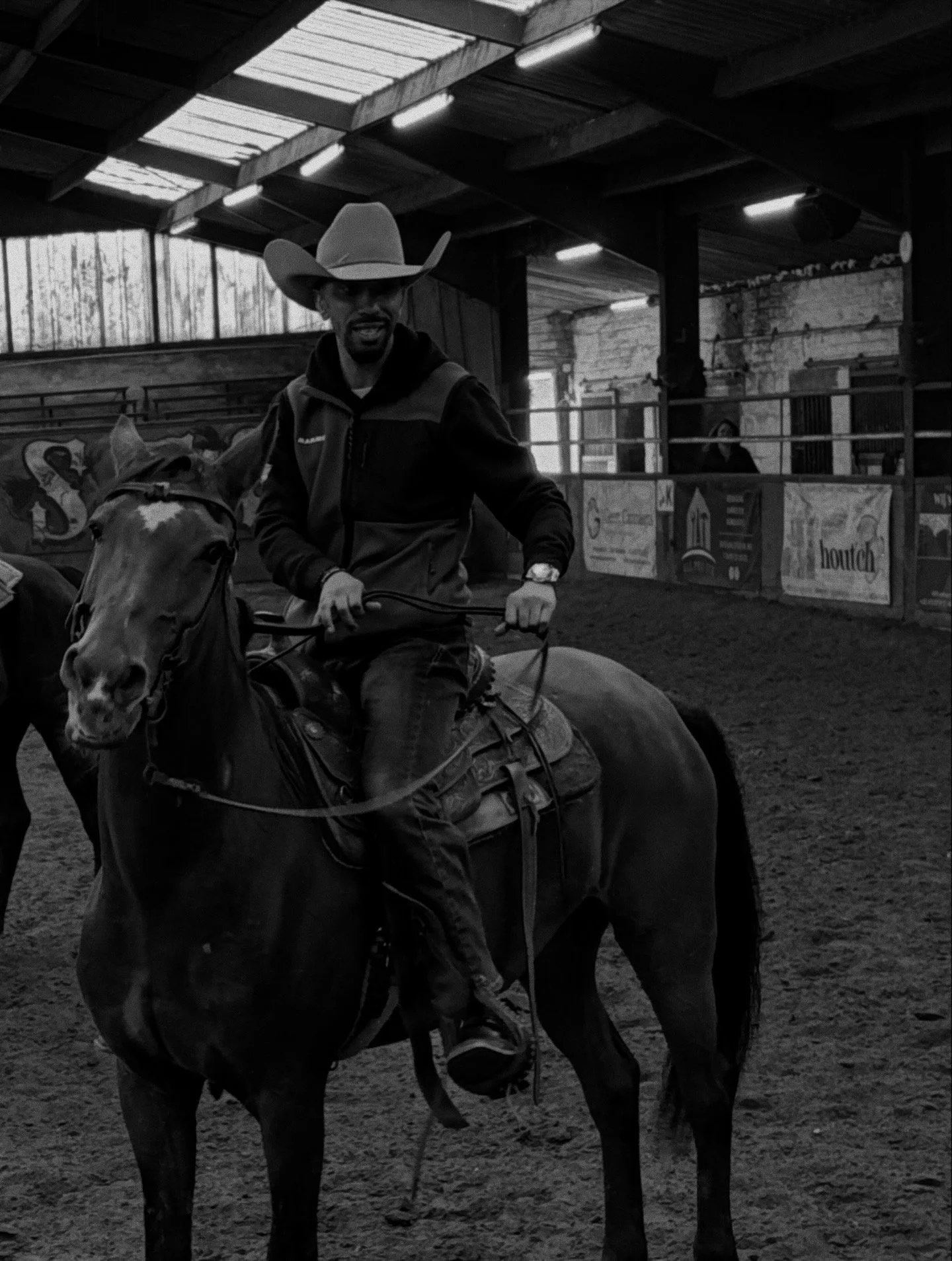 A man wearing a cowboy hat and riding a horse inside an indoor arena.