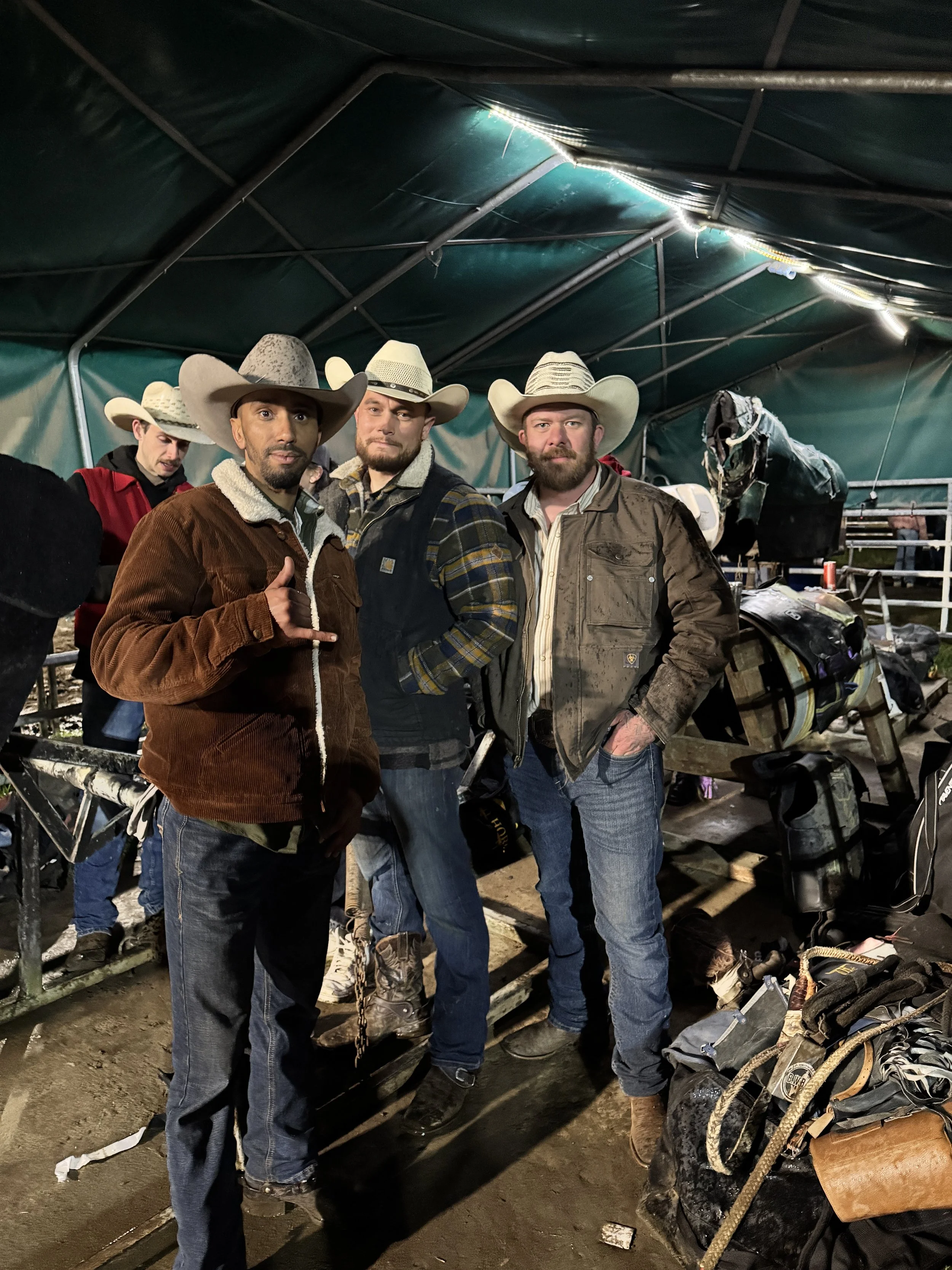 Three men wearing cowboy hats and casual country work attire standing inside a large green tent with equipment and supplies around them.
