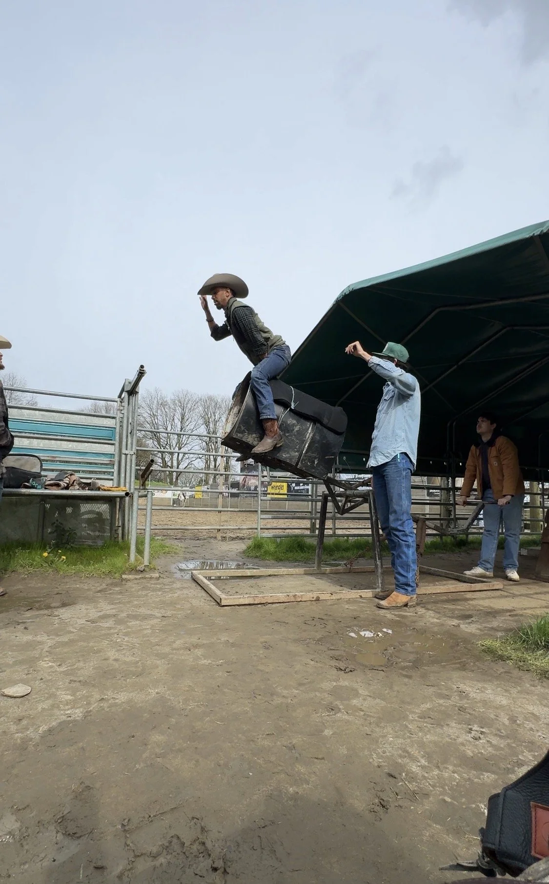 A person jumping onto a padded target during a rodeo event, with two others assisting nearby under a green canopy at an outdoor rodeo arena.