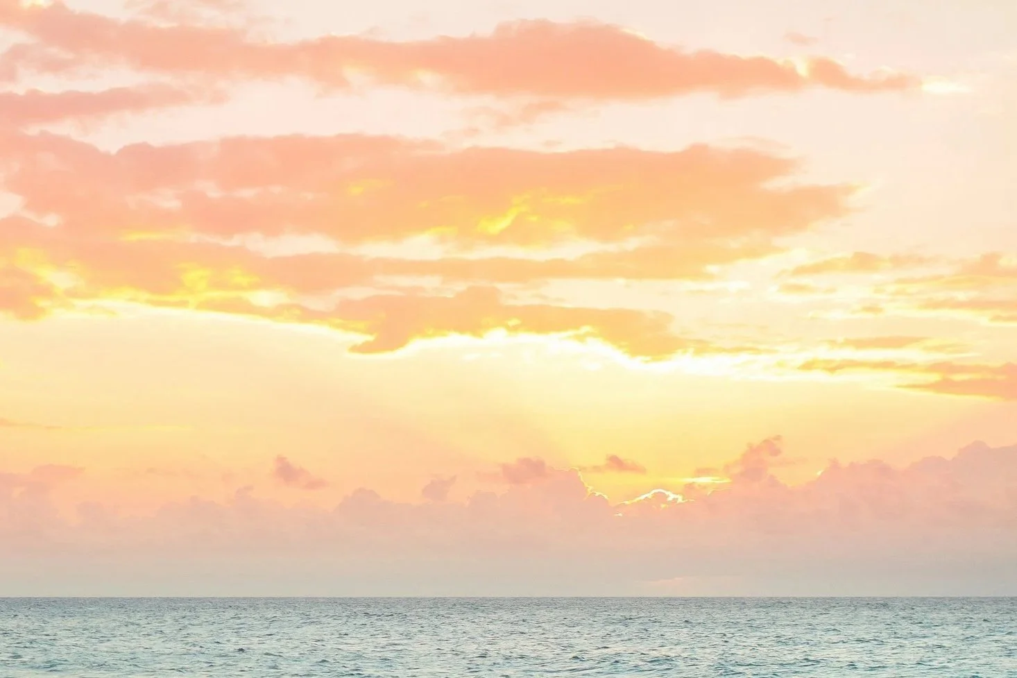 Sunset over the ocean with pink and orange clouds.