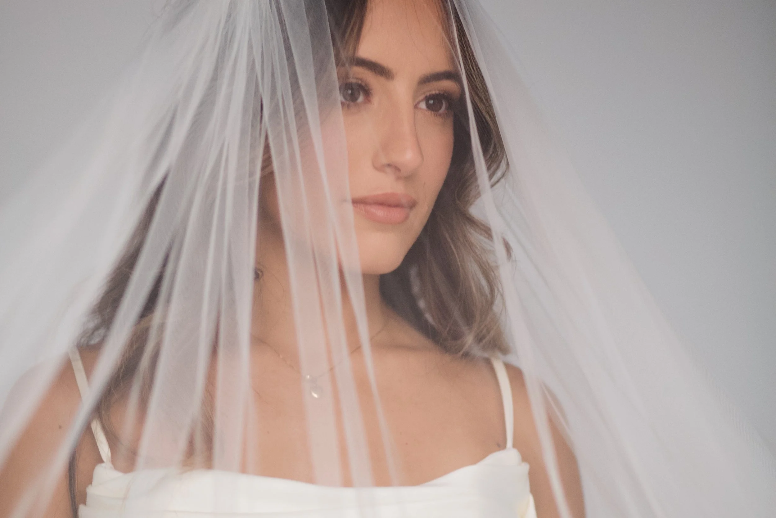 A bride wearing a white dress and veil, looking softly into the camera.