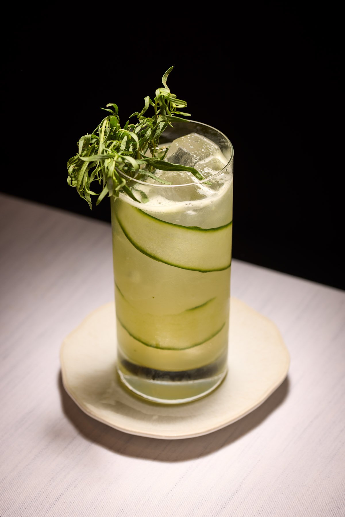 green cocktail in highball glass with sliced cucumber and green leafy garnish